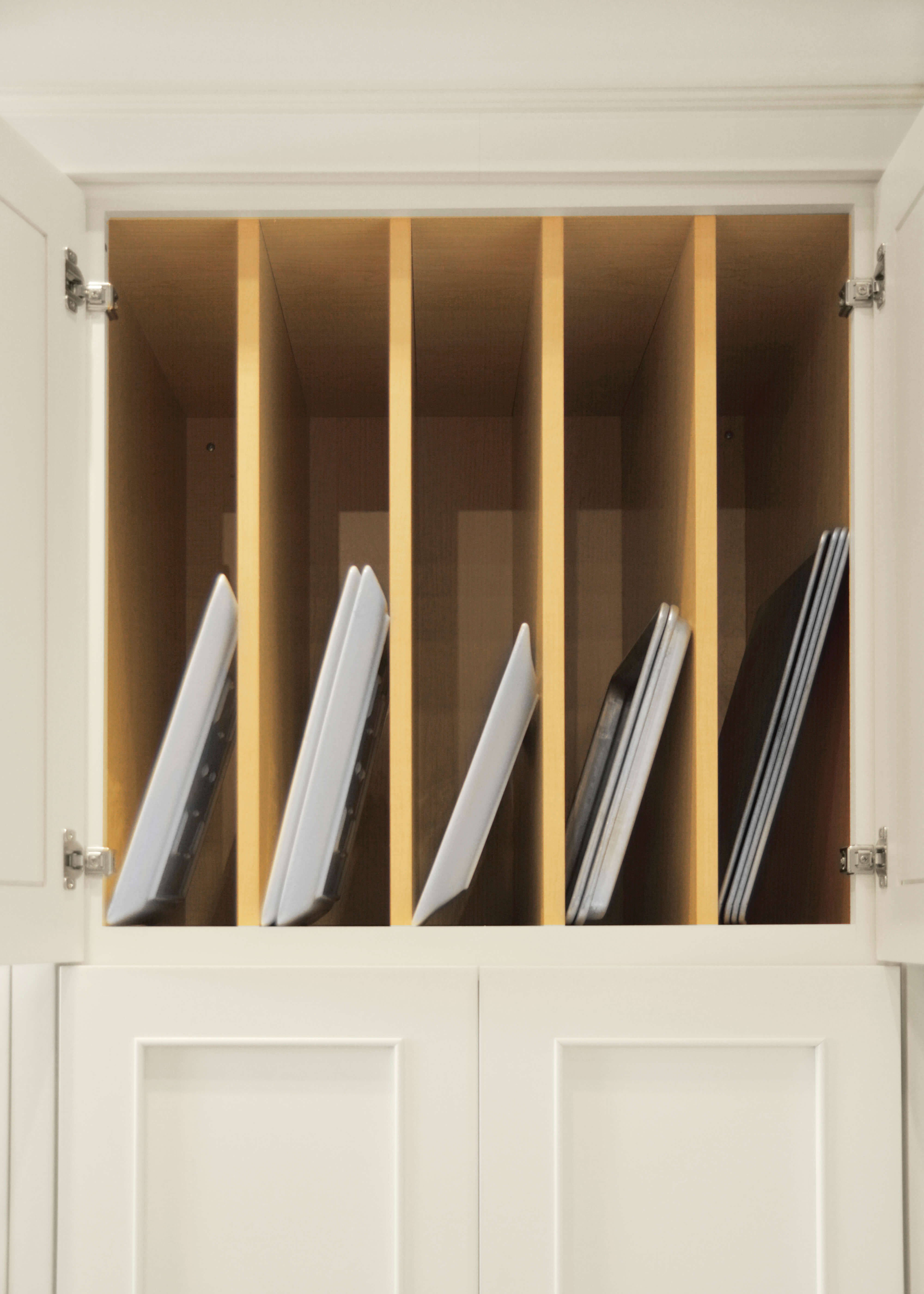 Cabinet partitions are used to create organized try and pan storage in an upper wall cabinet. The kitchen cabinets have a transitional style with a white paint factory finish.