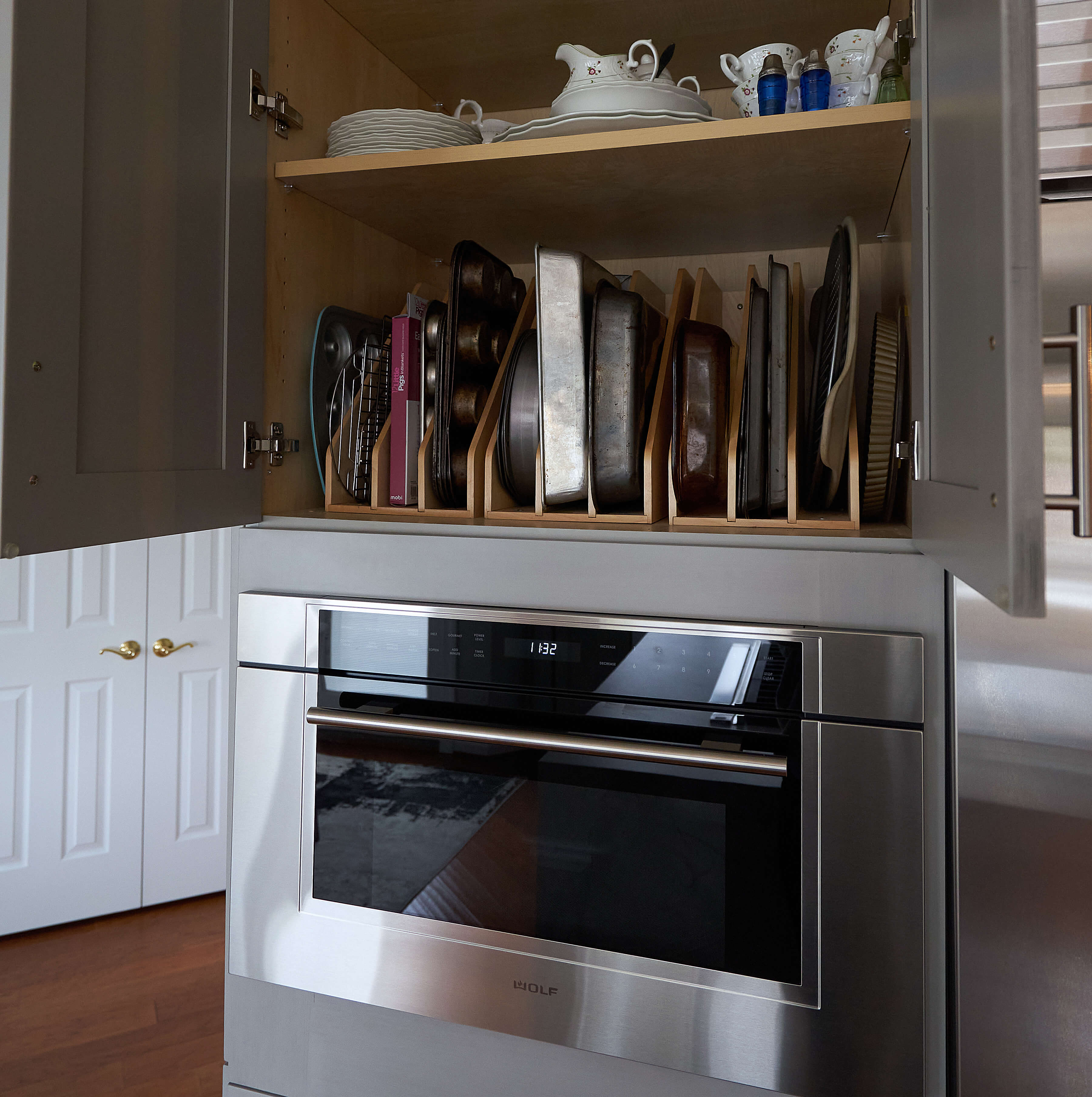 A cabinet above a wall oven with several tray dividers for organizing baking sheets, pizza pans, muffin tins, cutting boards, and trays.