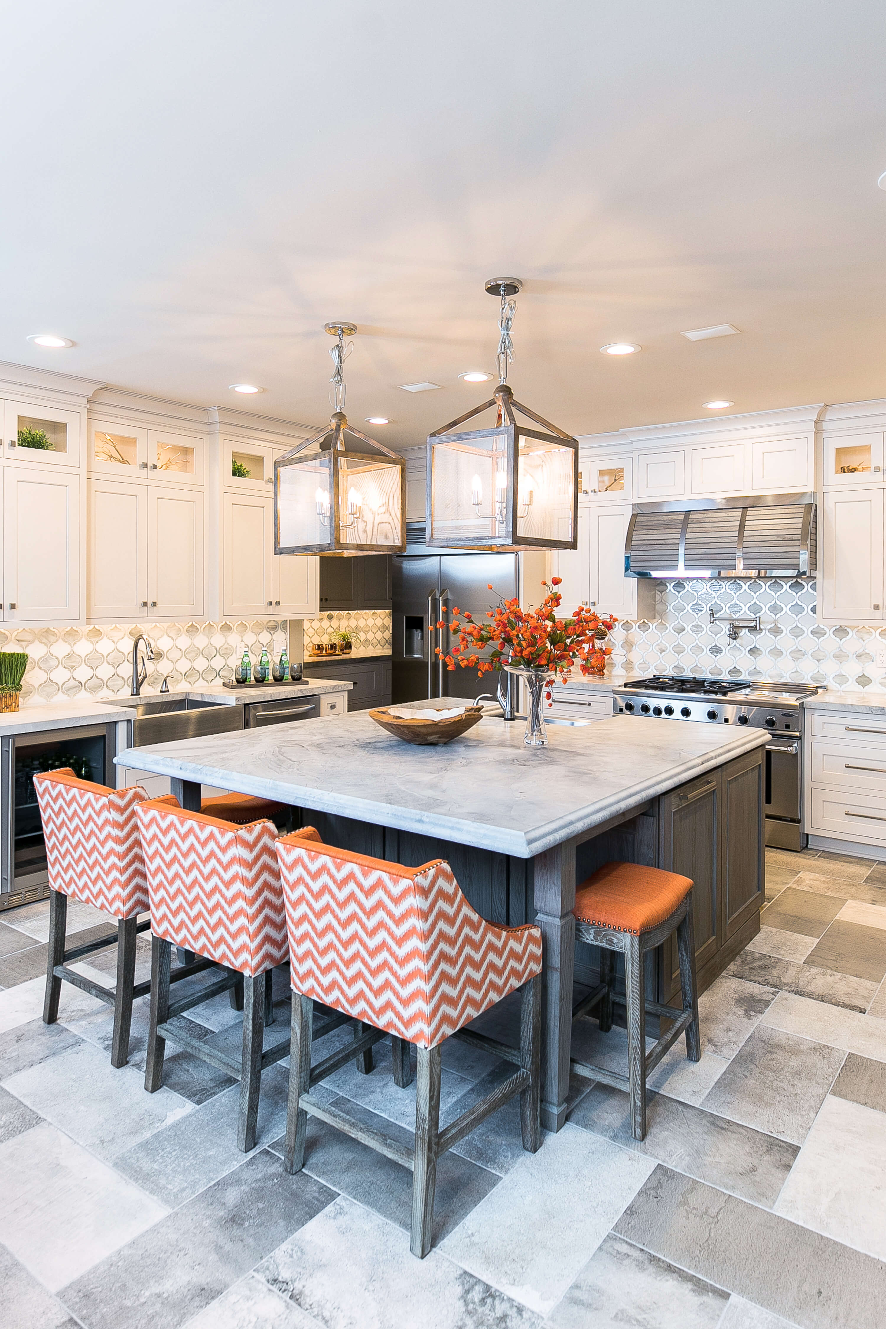 A square kitchen island with weathered wood cabinets and orange stools surrounded by white shaker cabinets for the perimeter.