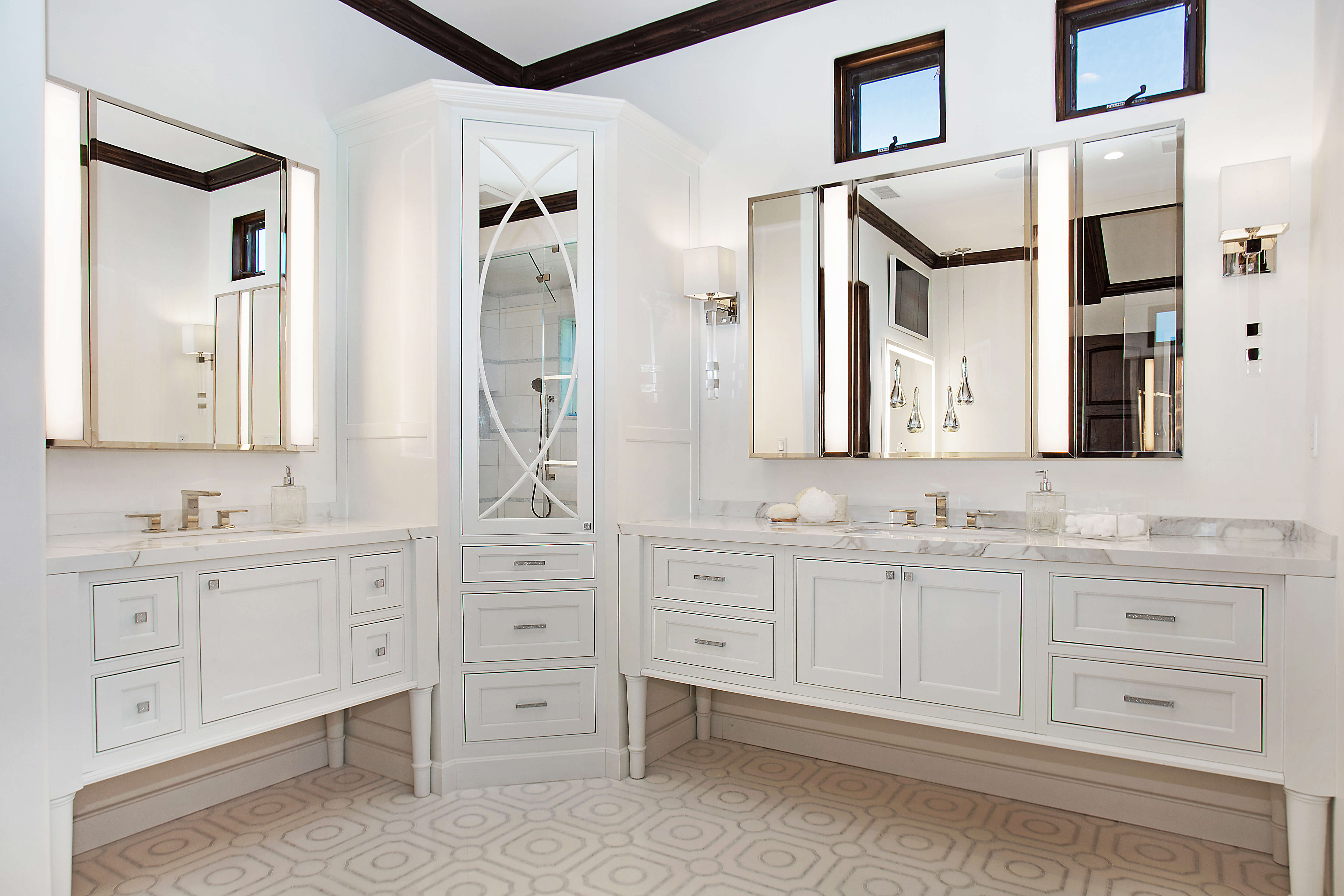 A corner double vanity with dual sinks on opposite separate walls. A tall mirrored linen cabinet sits in the corner dividing the two vanity spaces.