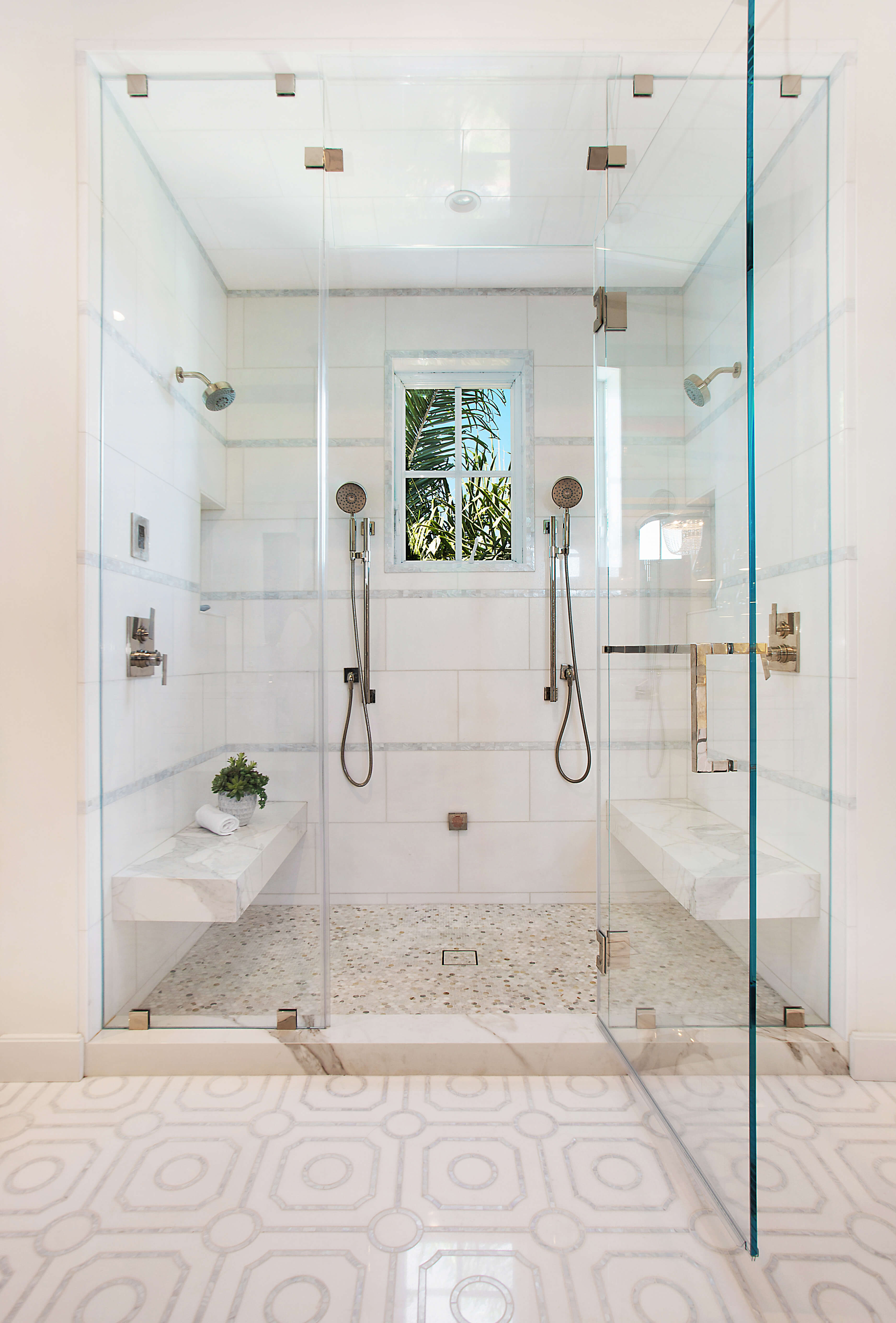 An all white shower with glass doors with multiple shower heads.