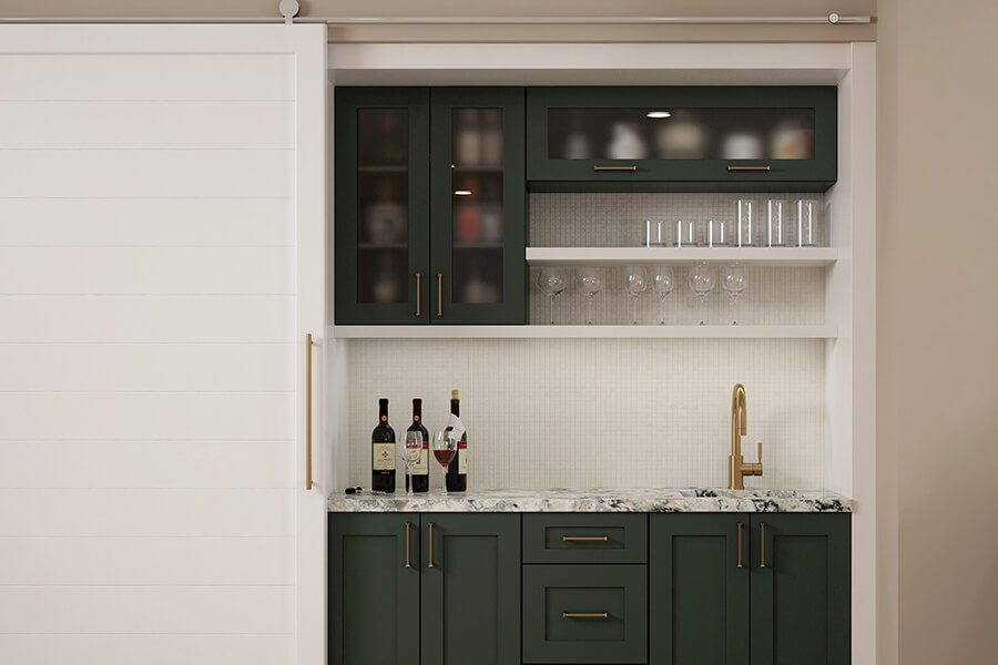 A dark green wet bar nook hidden behind a shiplap barndoor with brushed brass hardware and fixtures. .