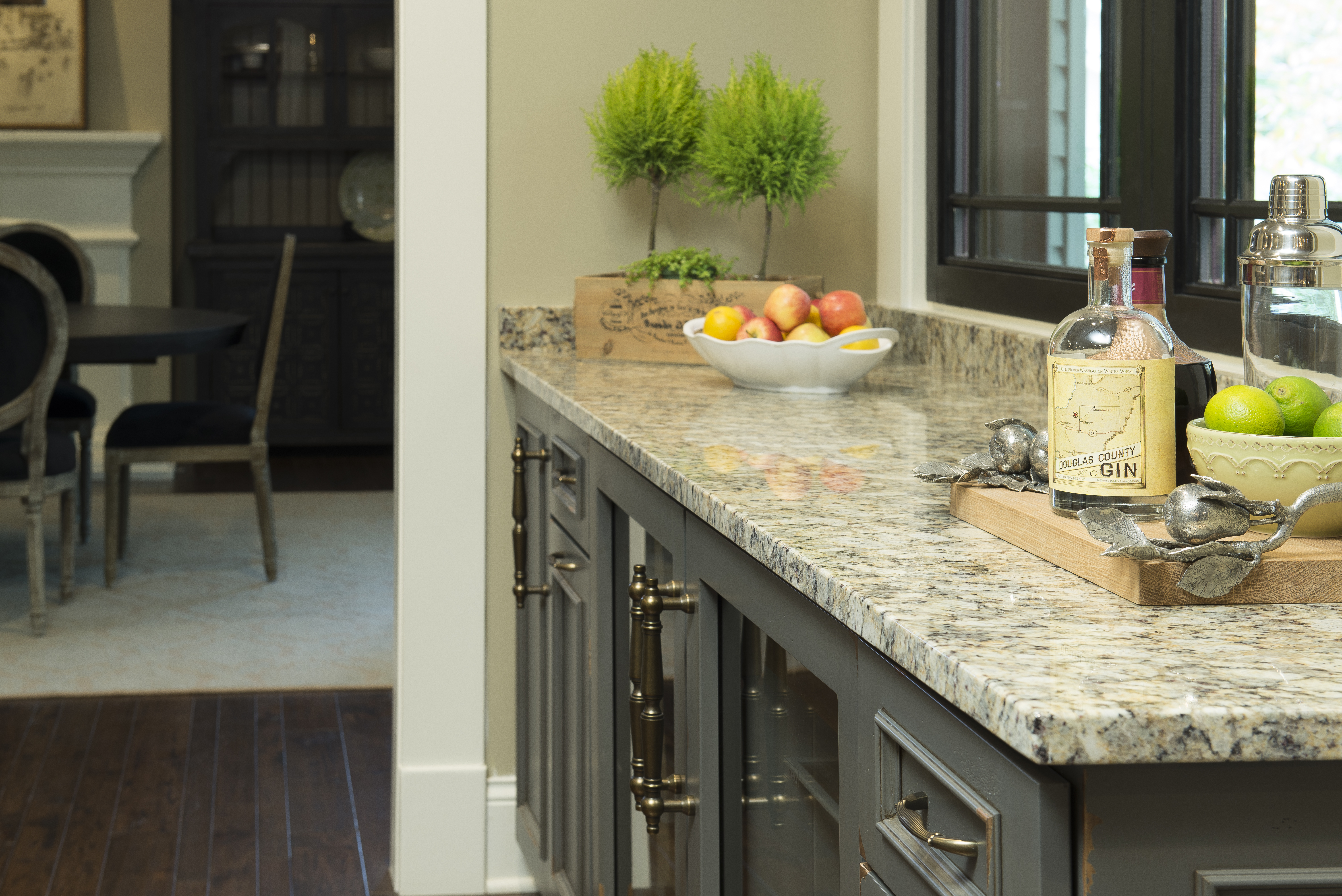 A beautiful wet bar area with kitchen cabinets that have a painted finish with distressed details. The dark gray paint is a classic kitchen cabinet color and pairs well with the traditional granite countertops.