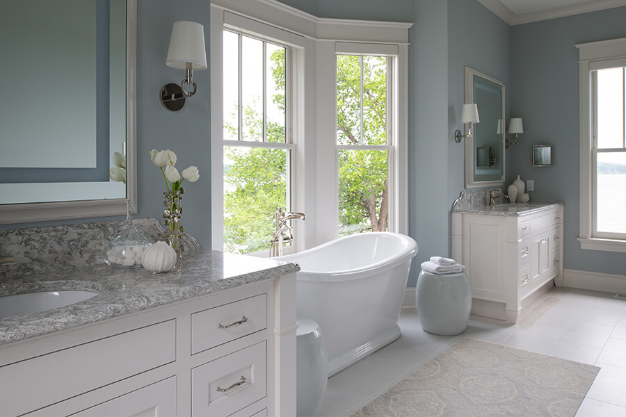 A beautiful transiitional and coastal master bathroom with two white furniture vanities.