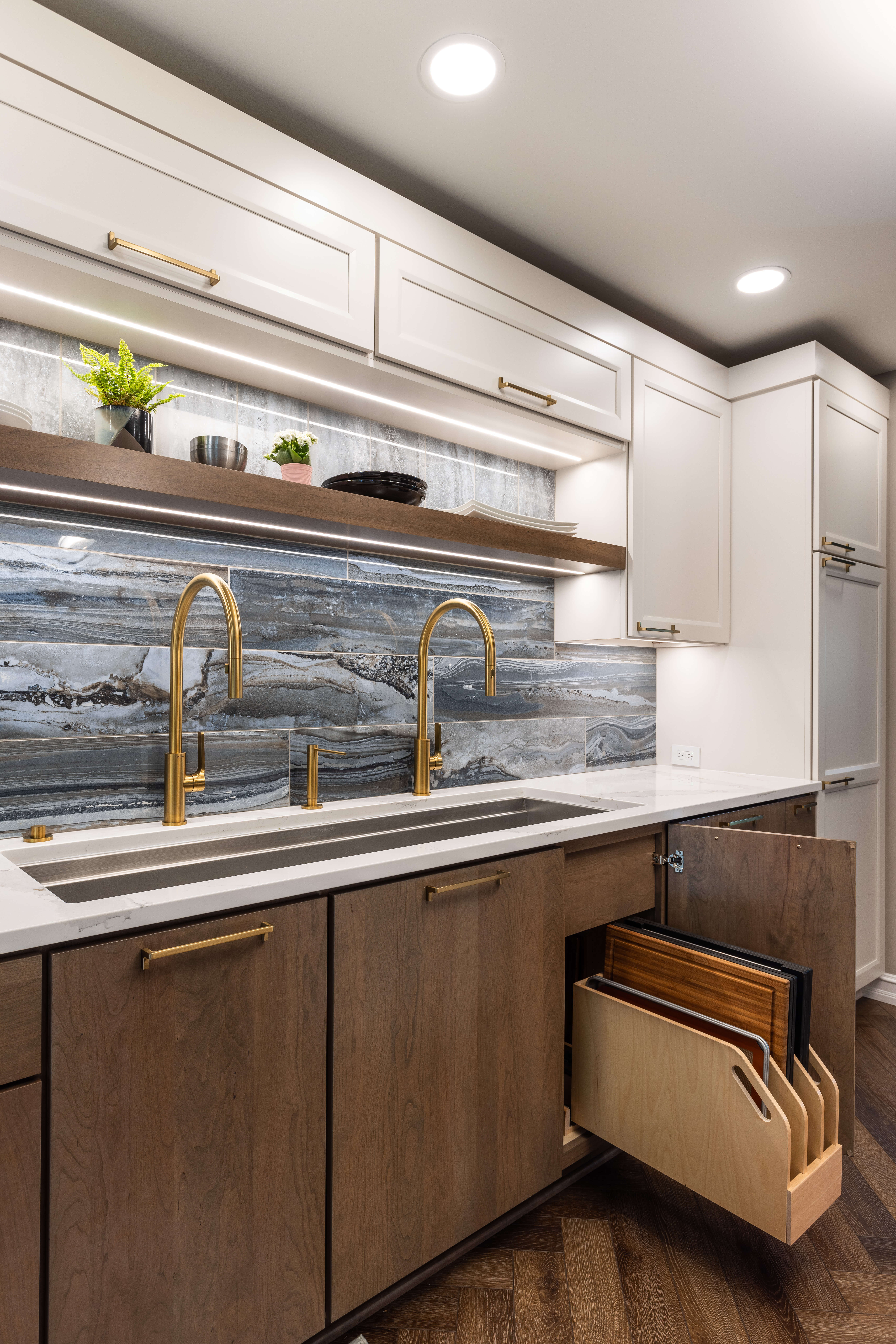 A two-toned kitchen with a medium stain and an off-white paint for the cabinets features a pull-out storage accessory for tray storage.