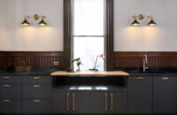 A wall with only base cabinets in a dark charcoal gray paint with skinny shaker door styles with a shelf across the window.