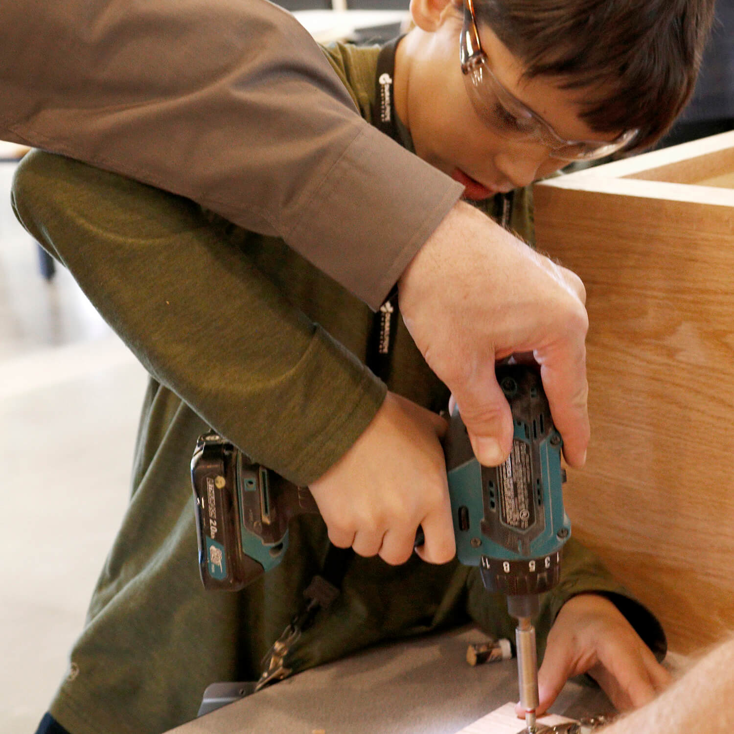 Student learning how to use a power drill to put on hinges of a cabinet.