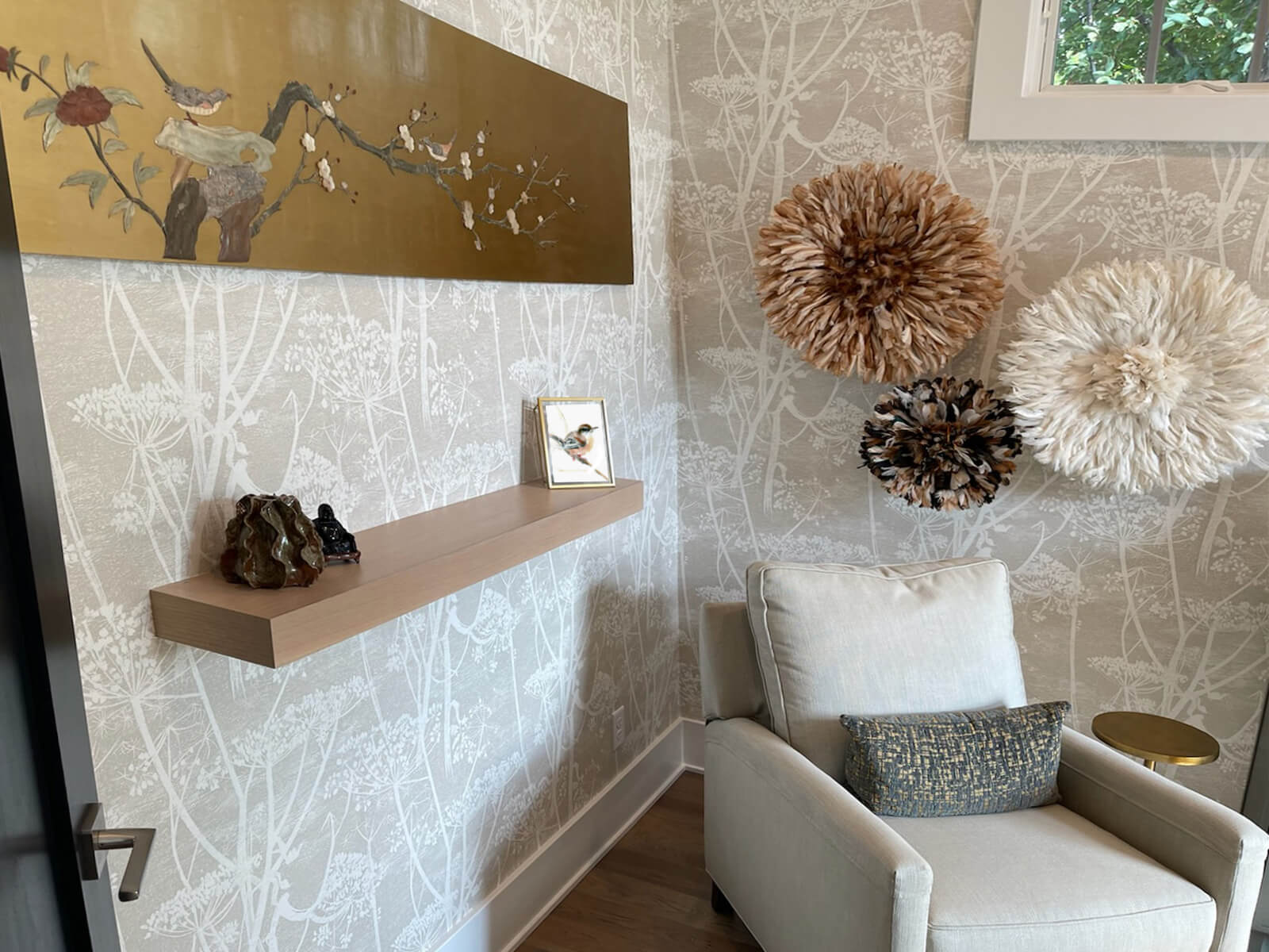 A floating shelf mounted below the wall art next to a lounge chair creates a beautiful sitting area of guests and clients who visit this pretty home office.