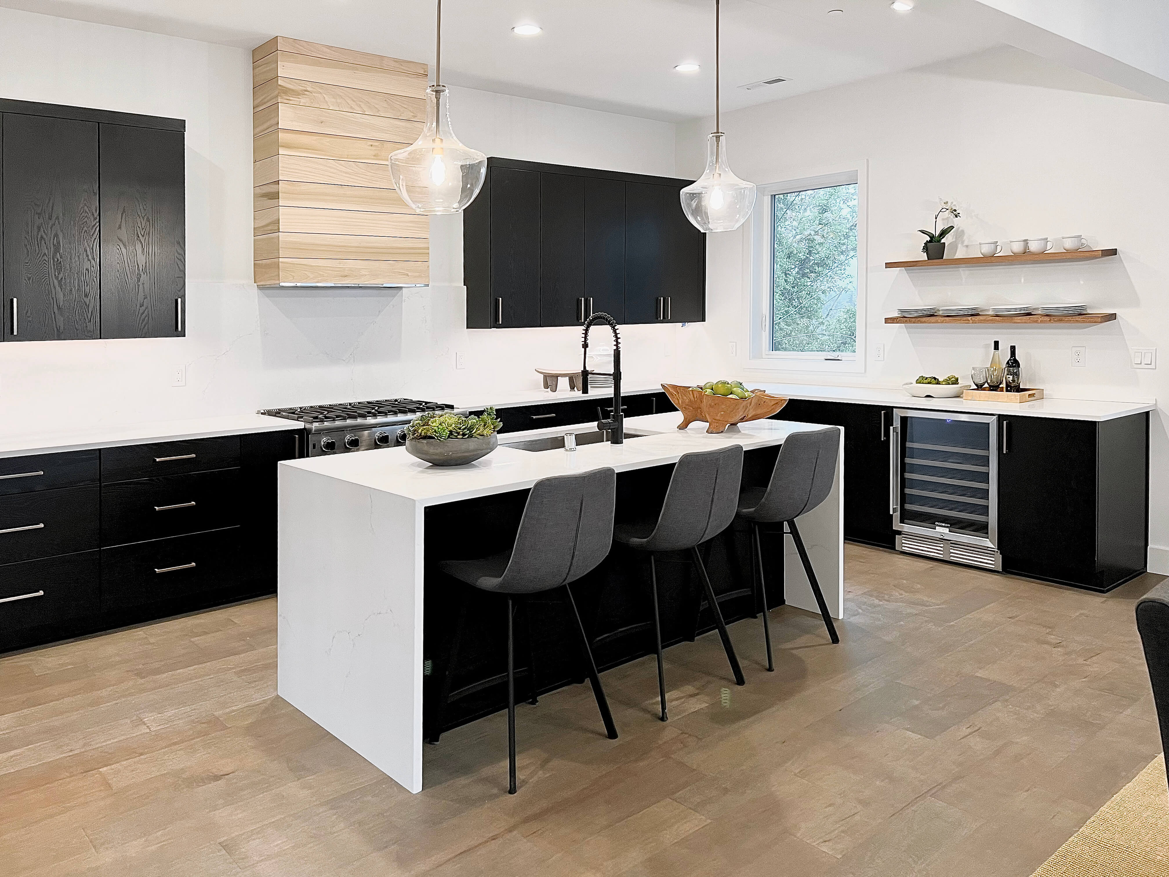 A black and white contemporary kitchen with a light stained shiplap wood hood featuring black painted oak cabinets with a modern slab door style.