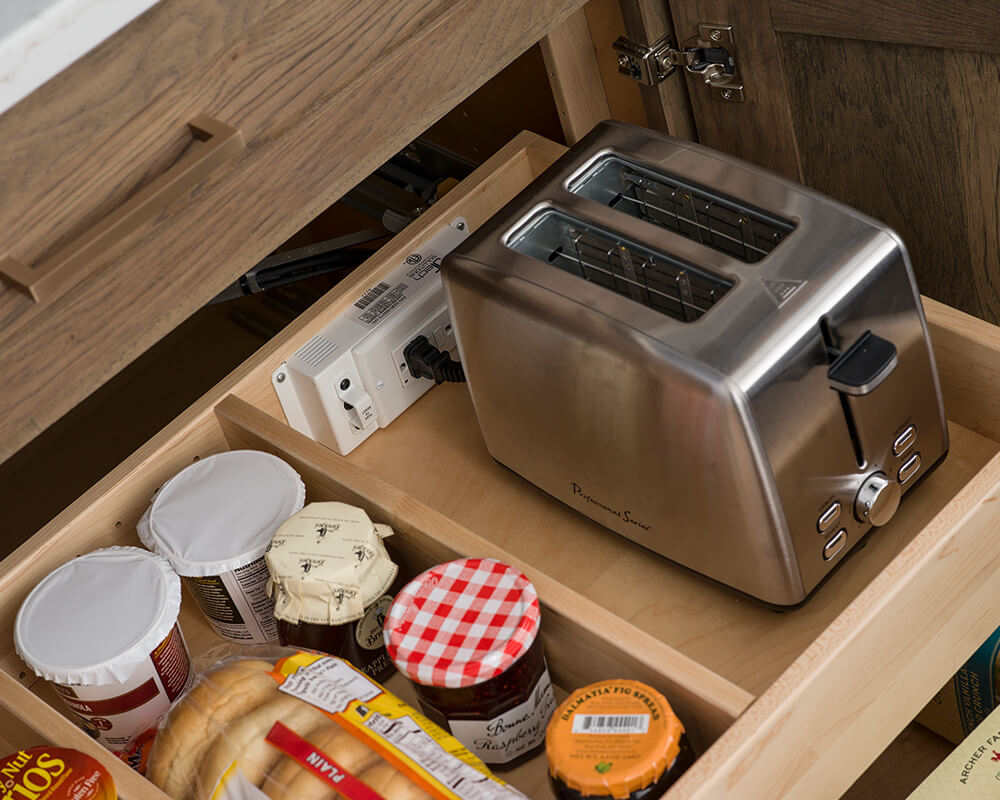 A roll-out shelf in a cabinet with a built-in outlet for toaster storage and use.