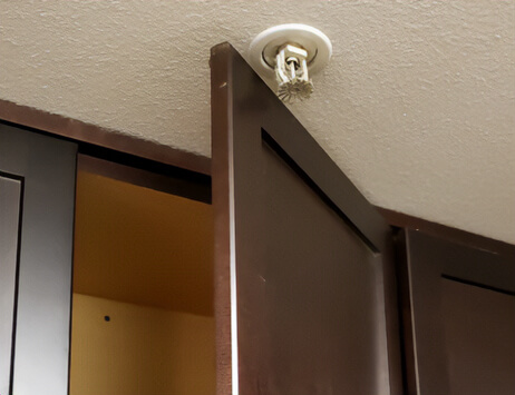 In this terrible kitchen design, a sprinkler alarm on the ceiling gets clunked by the cabinet door every time it opens.