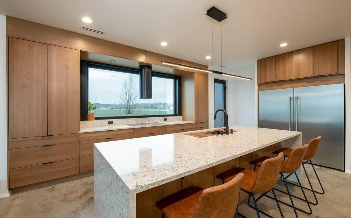 A warm & contemporary kitchen with black accents, white countertops, and light stained Quarter Sawn White Oak cabinets with a slab door style.
