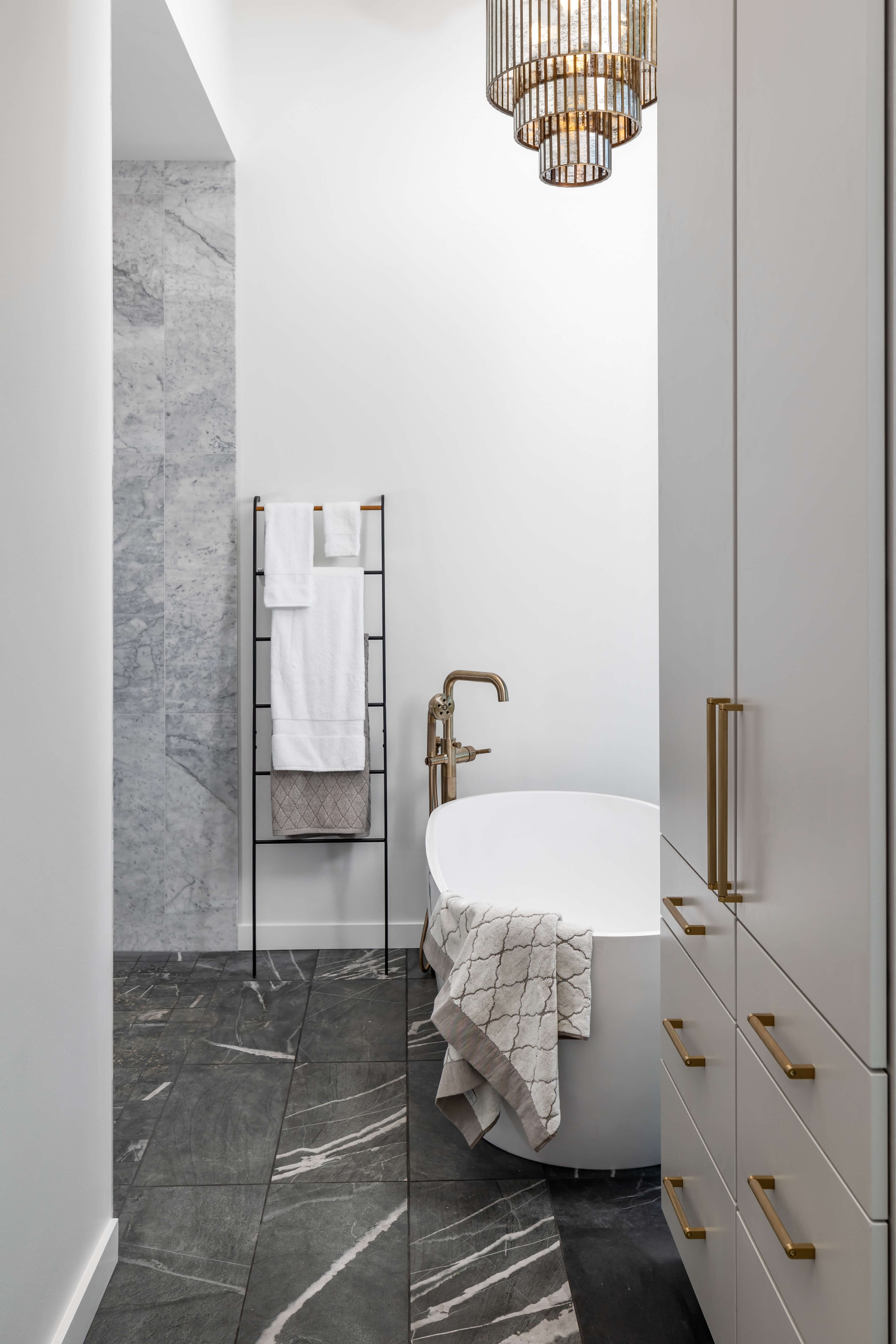 A beautiful spa-like master bathroom with a freestanding tub and tall light gray/off-white linen cabinets with brushed brass hardware.