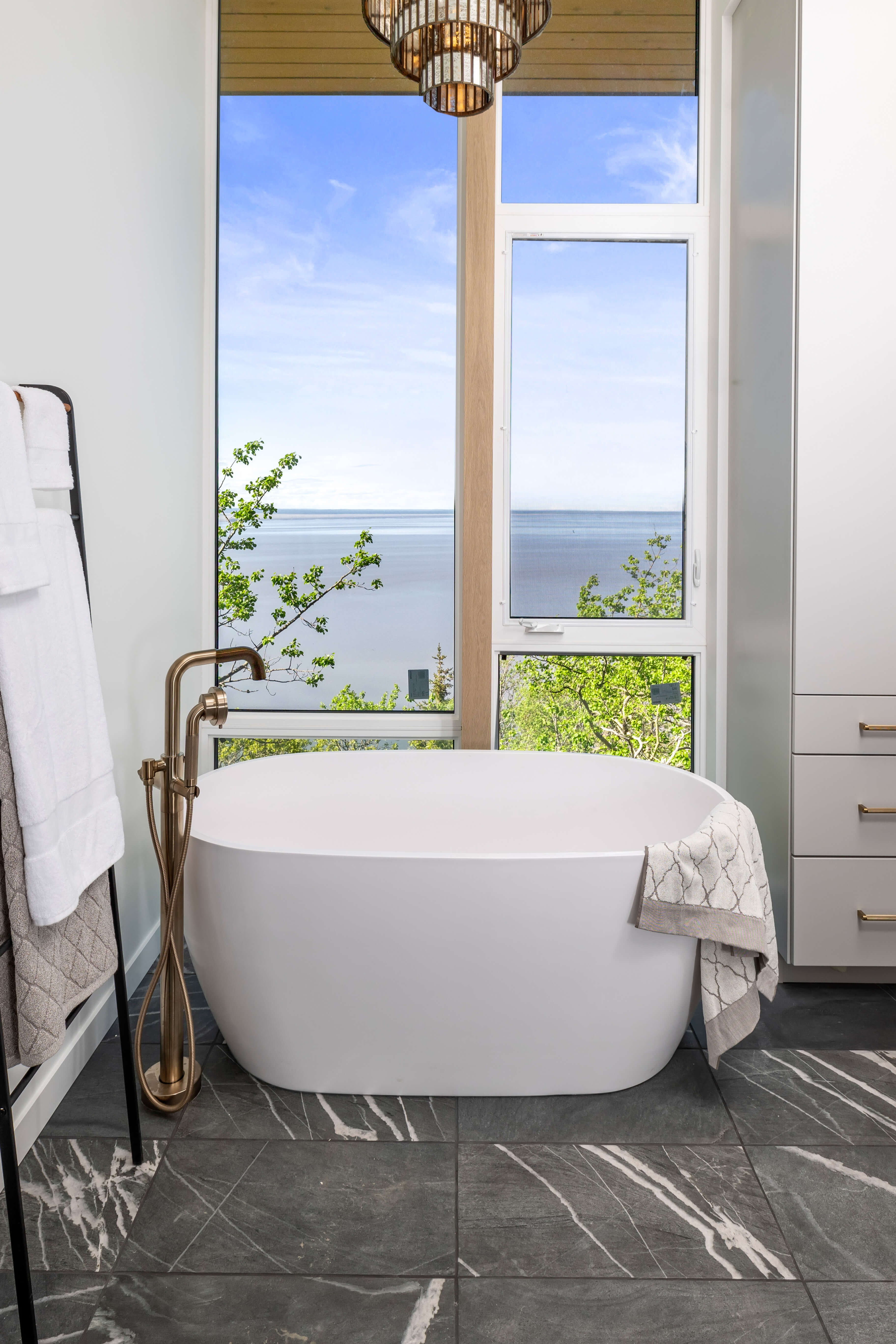 A master bathroom with a stunning window view from the freestanding soaking tub with tall linen cabinets from Dura Supreme.
