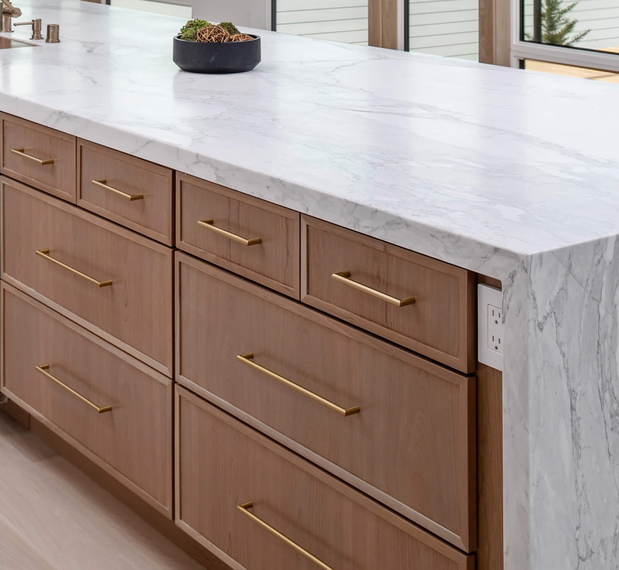 A kitchen island with light stained cherry cabinets with a modern door style with skinny rails and stiles paired with a white waterfall countertop.