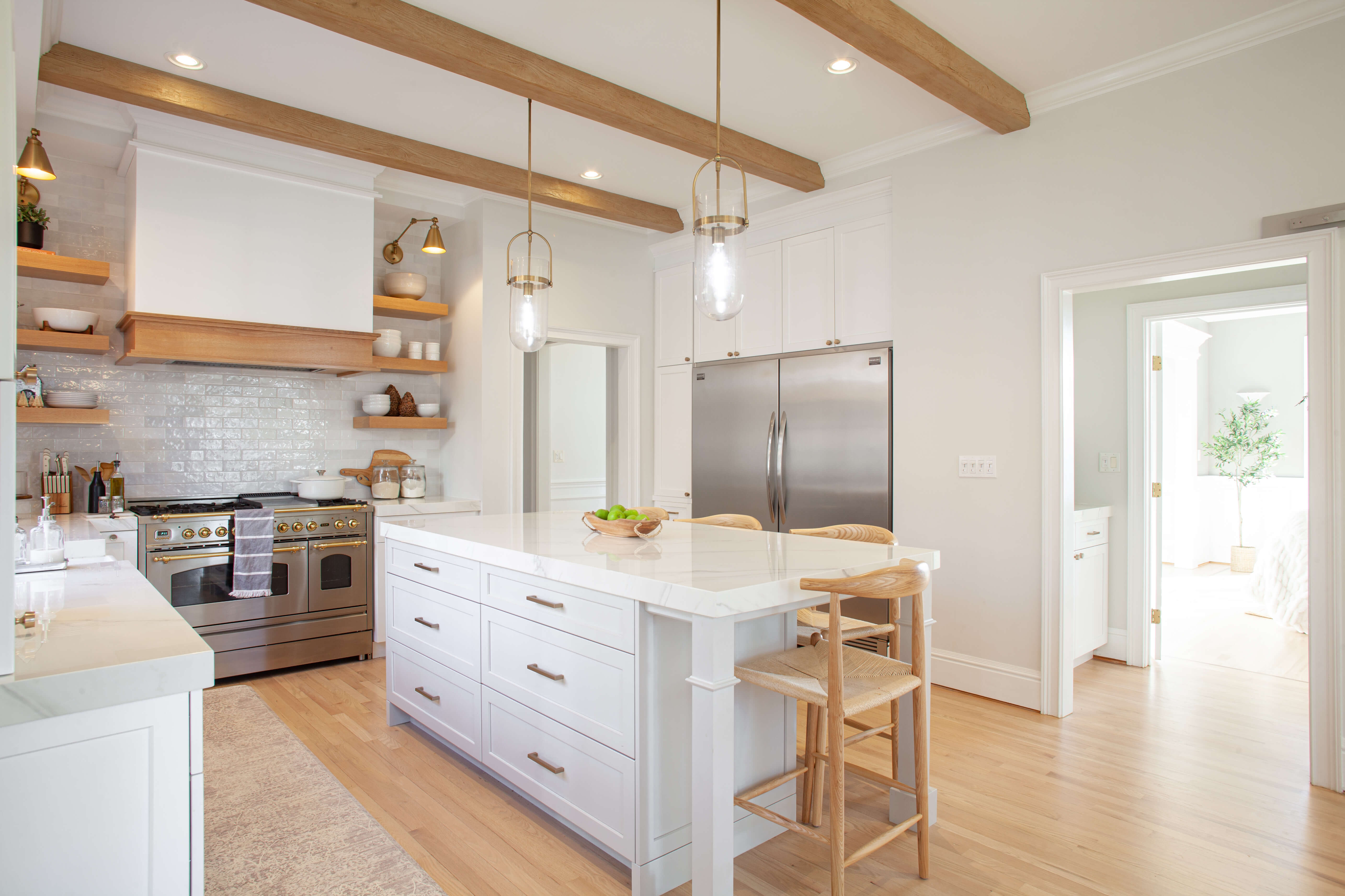 A beautiful white kitchen with light stained Quarter-Sawn White Oak accents for the wood hood frieze, floating shelves, and ceiling beams.
