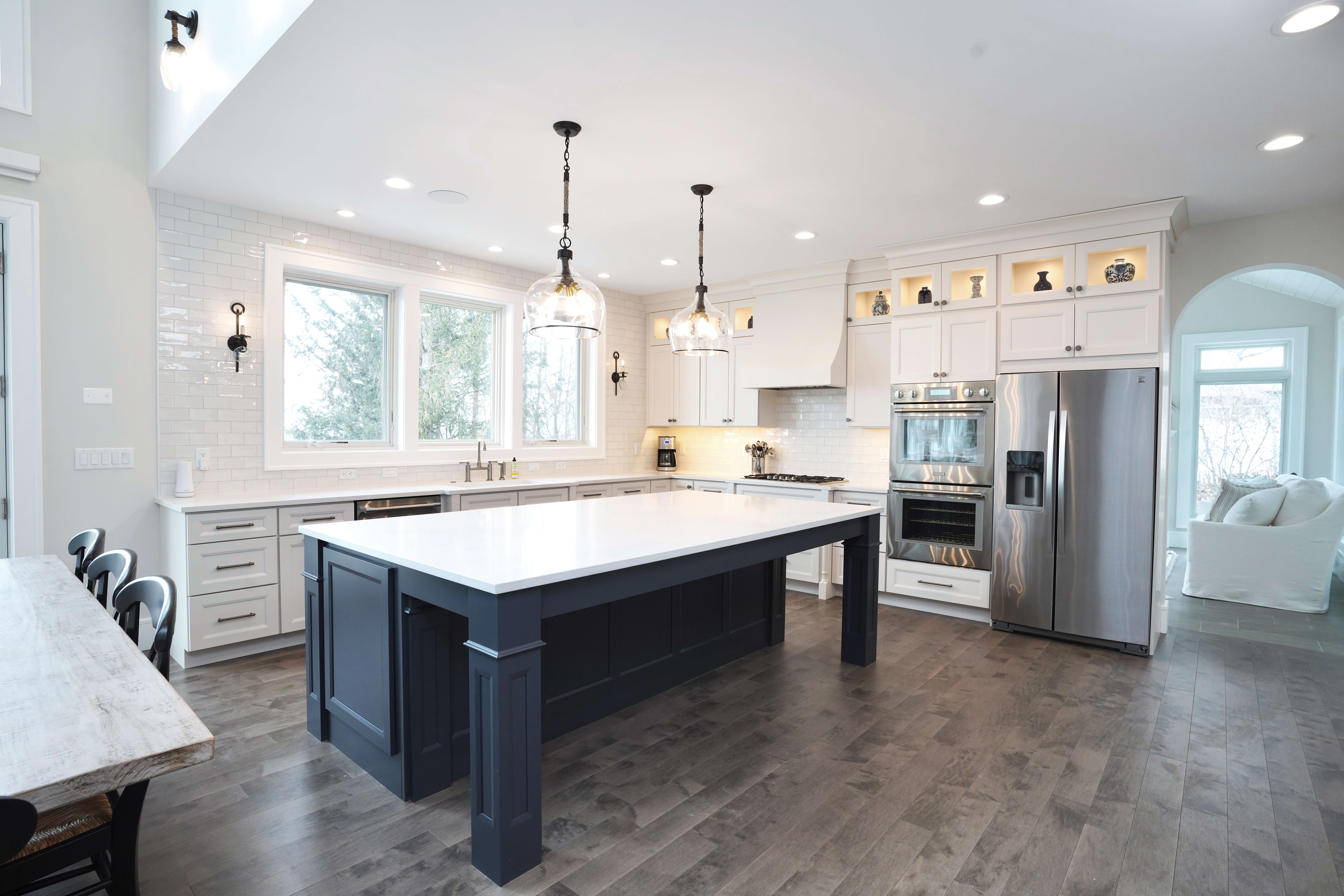 A smooth, dark navy blue painted kitchen island with column legs is the focal point in this open concept kitchen design with a perimeter full of white painted cabinetry.