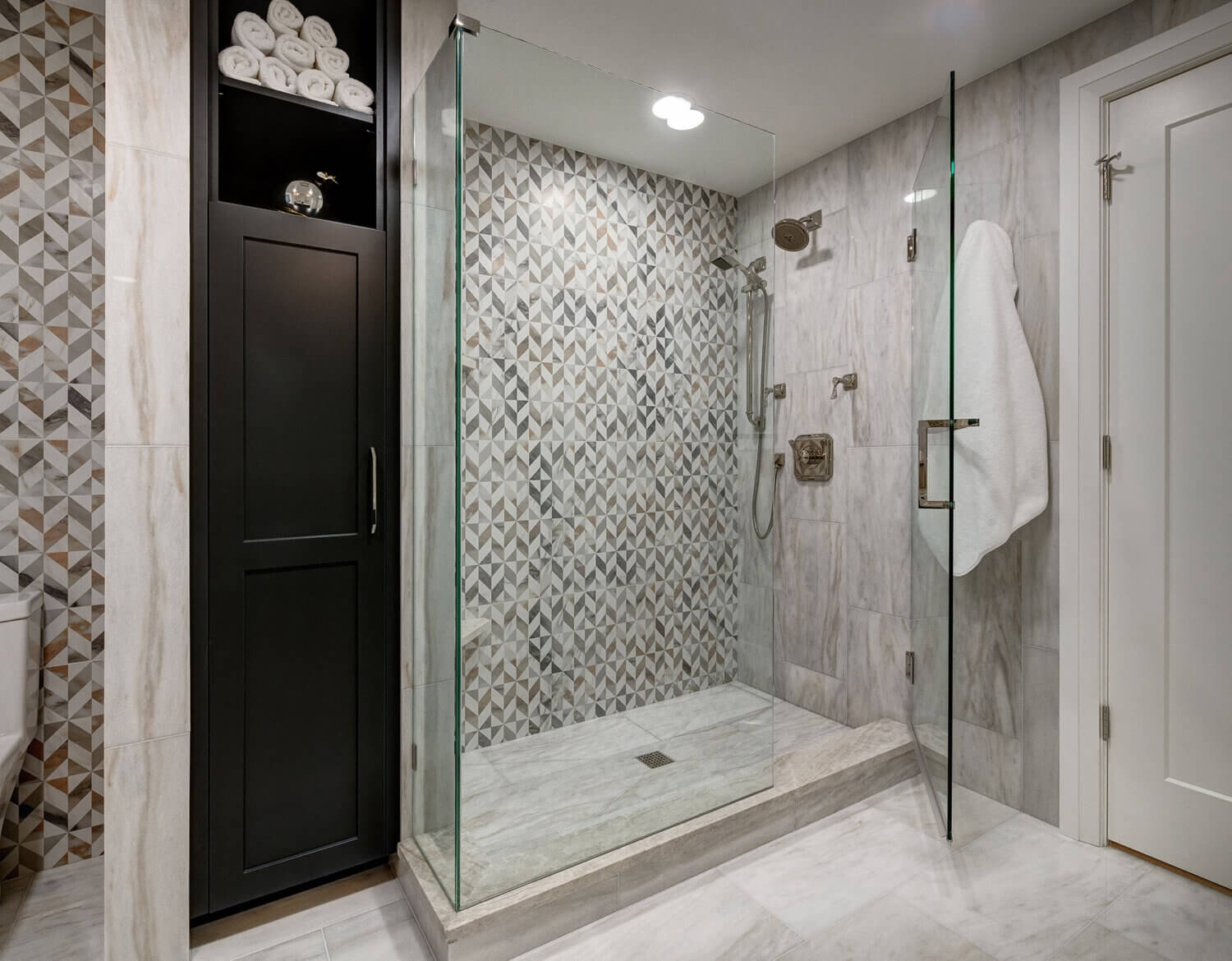 A built-in linen cabinet in black paint is set into the wall behind the walk-in shower creating a beautiful space for linen storage.