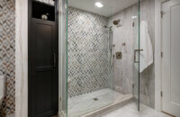 A built-in linen cabinet in black paint is set into the wall behind the walk-in shower creating a beautiful space for linen storage.