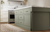 A green painted kitchen island with a furniture style look and slab inset cabinet doors with a beaded frame.
