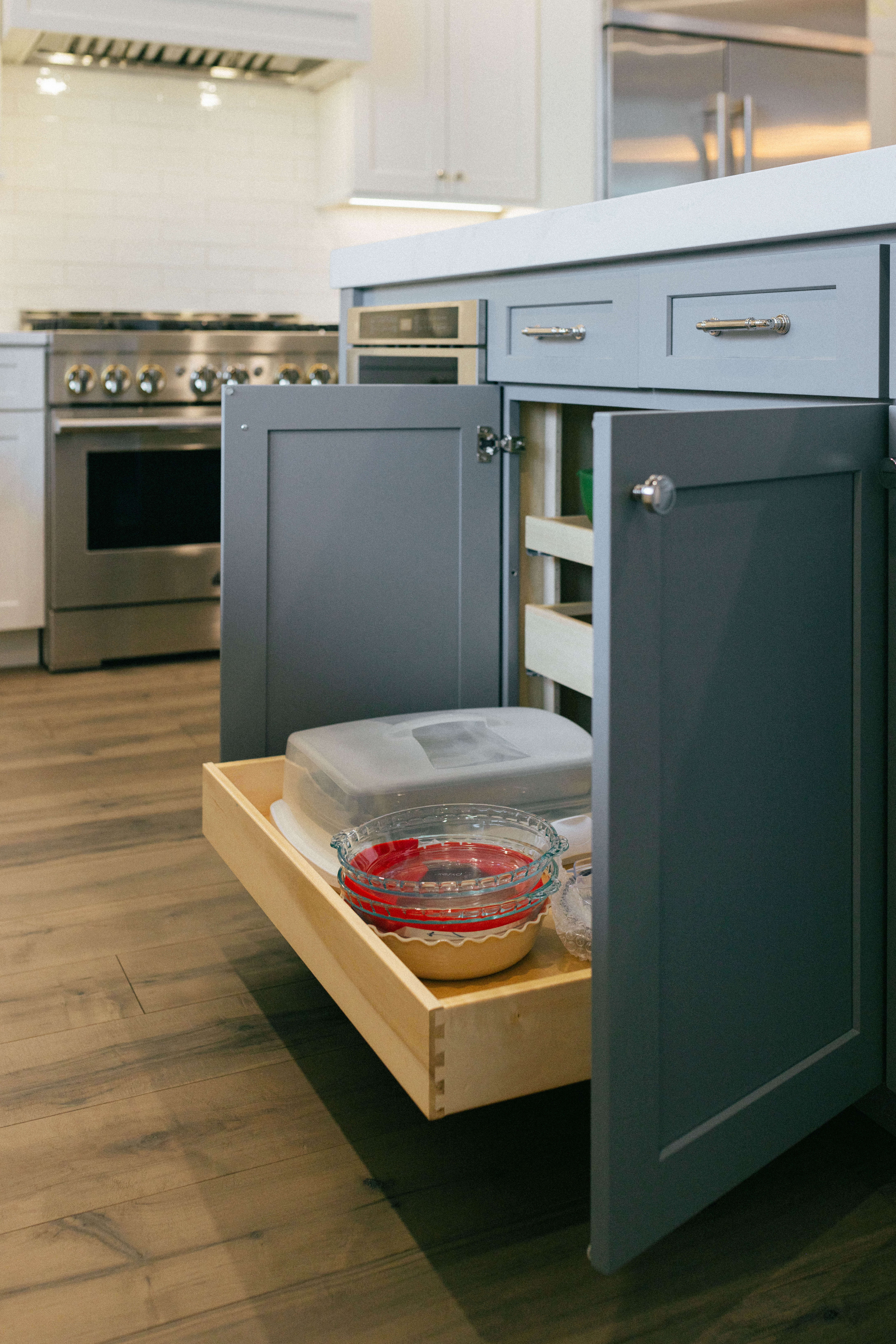 A dark gray painted kitchen island with roll-out shelf storage for baking containers and lids.
