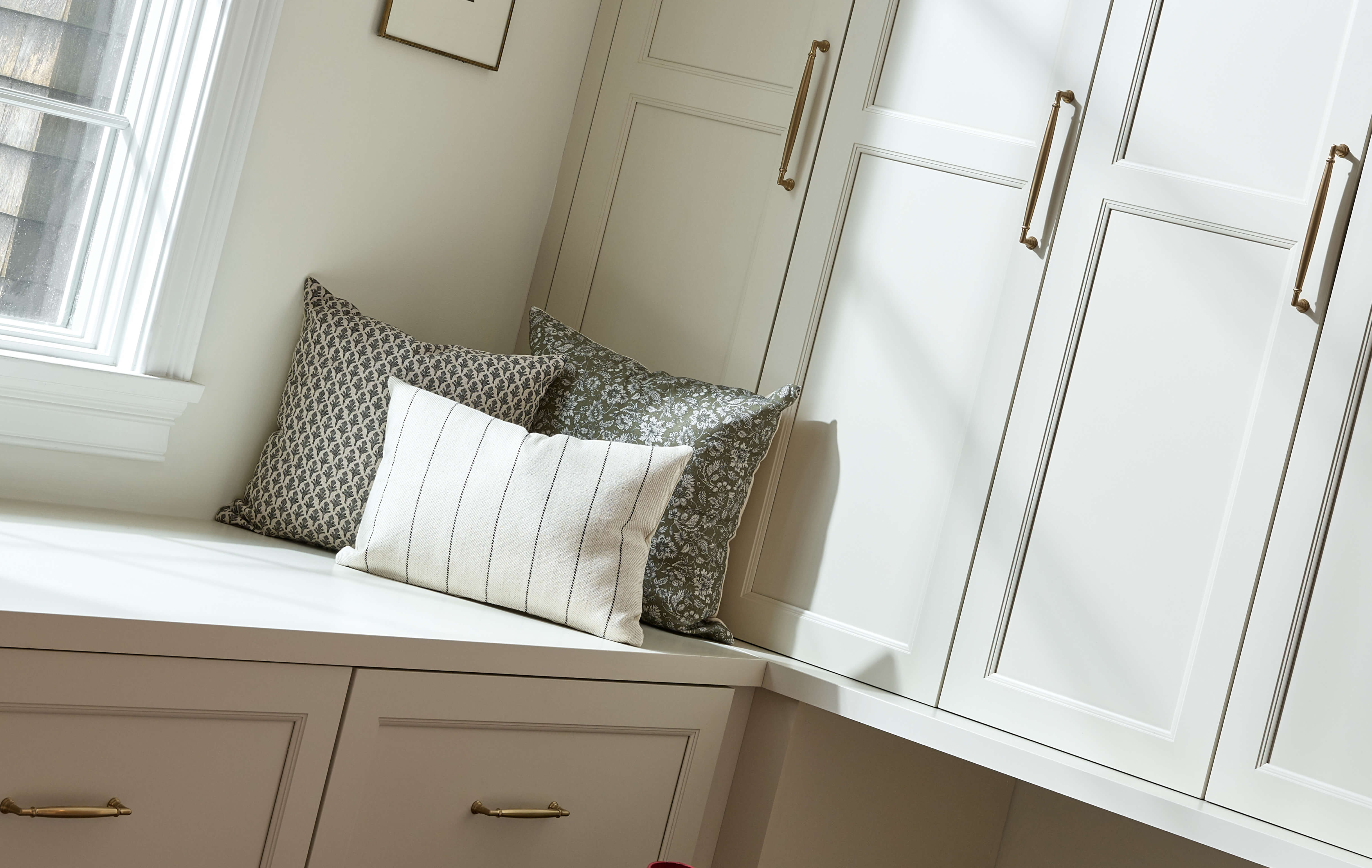 A closet design with a bootbench under a window and white painted cabinets from Dura Supreme.