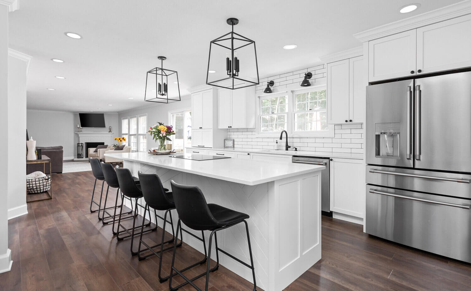 An all-white kitchen with black hardware, light fixtures, and bar stools. The back panel of the kitchen island features a unique shiplap pattern.