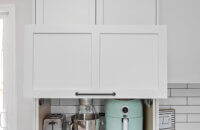 A larder cabinet with a lift-up cabinet door that hides several powered appliances at countertop level. Shown open.