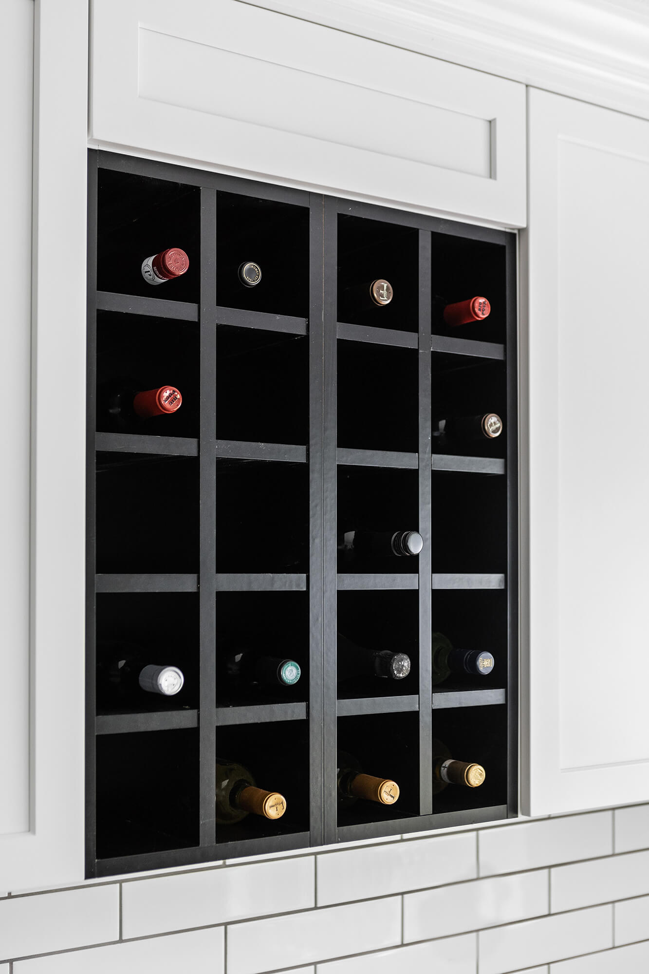 A close up of the black stained wall wine rack cabinet surrounded by bright white cabinets.
