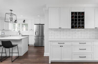 A bright, all-white kitchen with black accents including a black wine rack in a wall cabinet.
