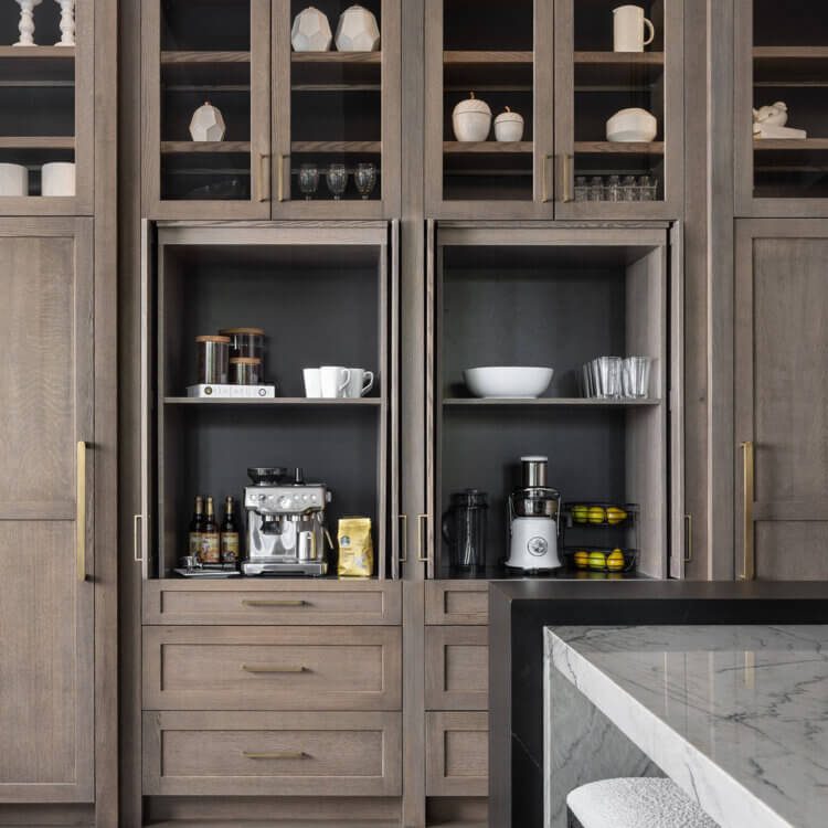 A pantry wall of cabinets with 2 hidden workstation larders. One houses everything needed for a coffee bar and the other everything for a smoothie station.