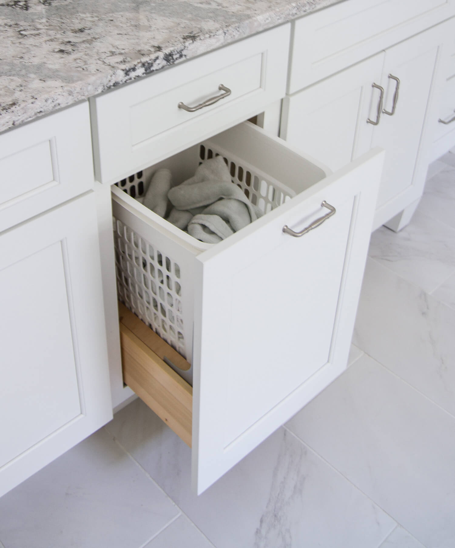 A bright white cabinet with a laundry bin pull-out storage accessory.