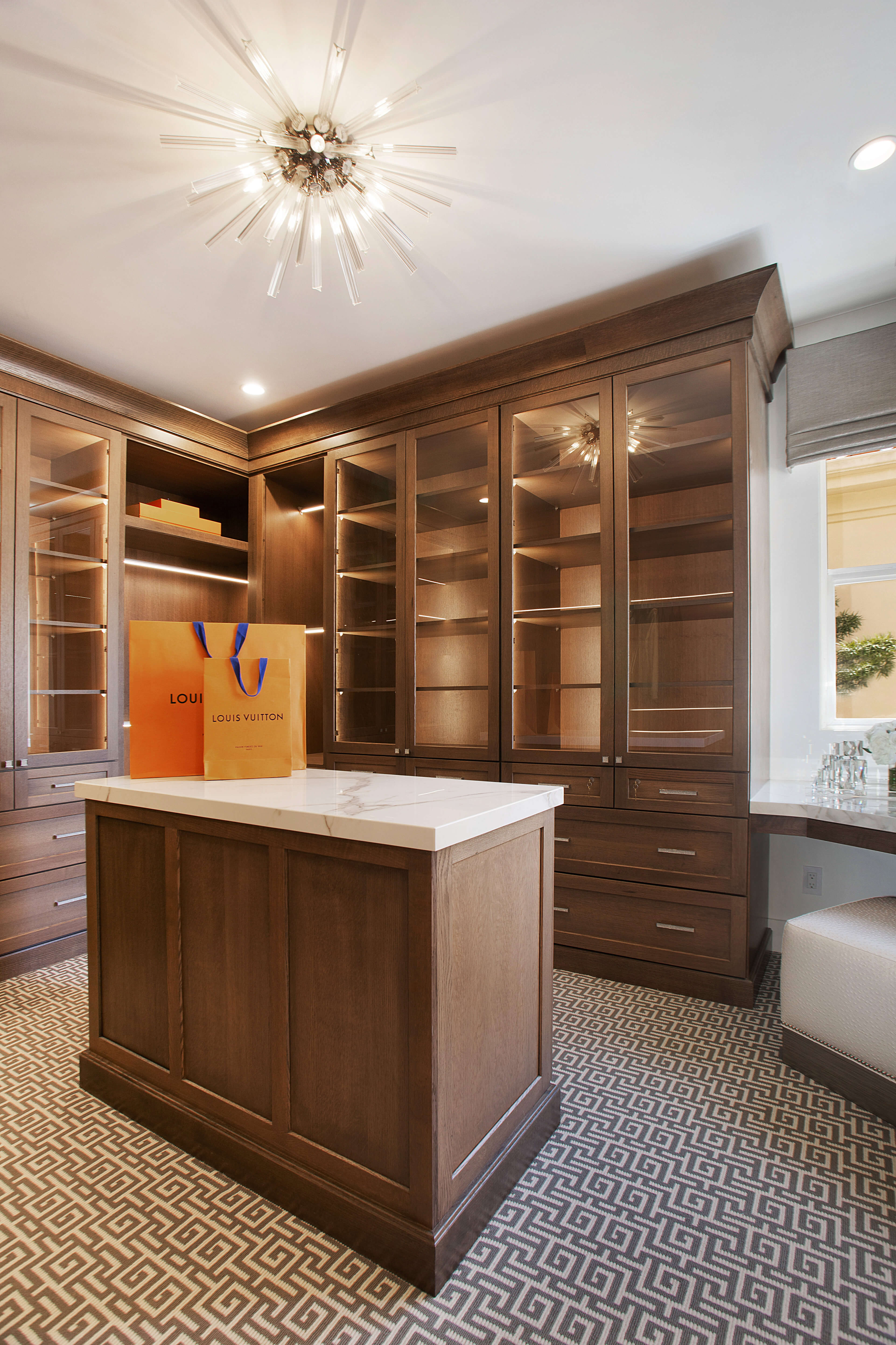 A custom walk-in closet design with an island, shelves for shoe, and an angled corner desk and beauty station.