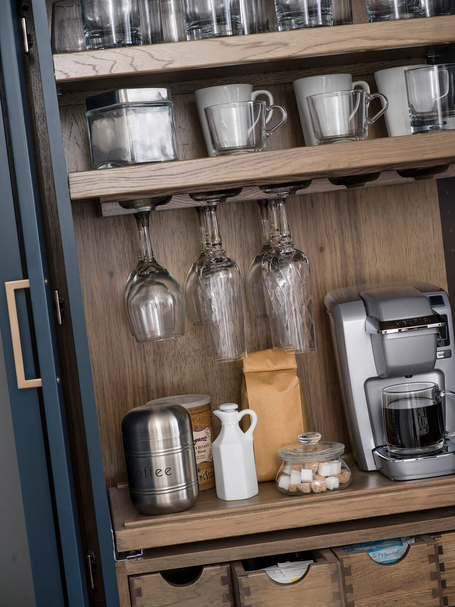 A beverage center larder cabinet with customized internal storage accessories including apothecary drawers, a flat roll-out shelf for a coffee maker or blender, and additional customized shelving.
