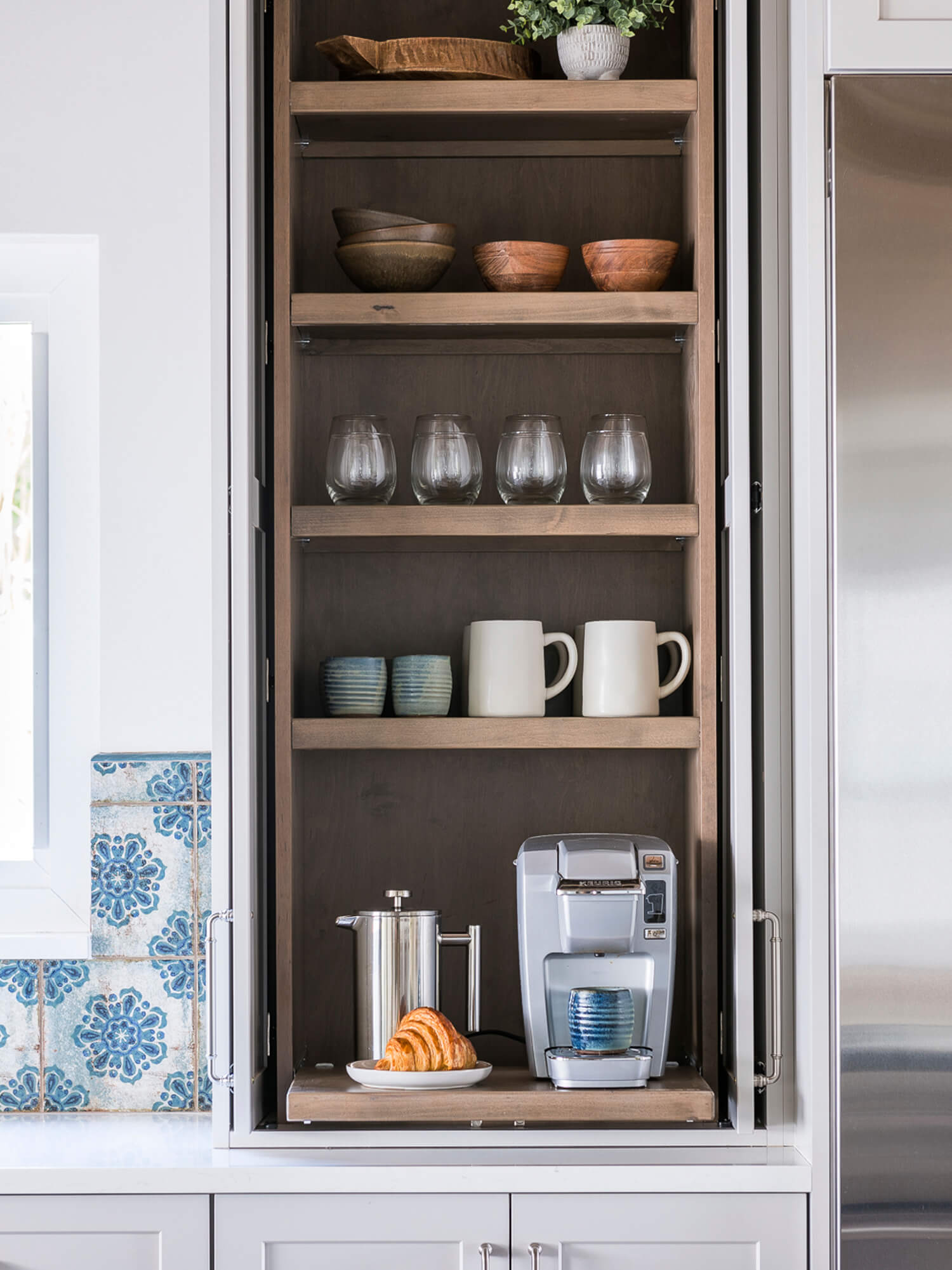 A tall and thin larder cabinet with pocket doors created to be a hidden coffee station.