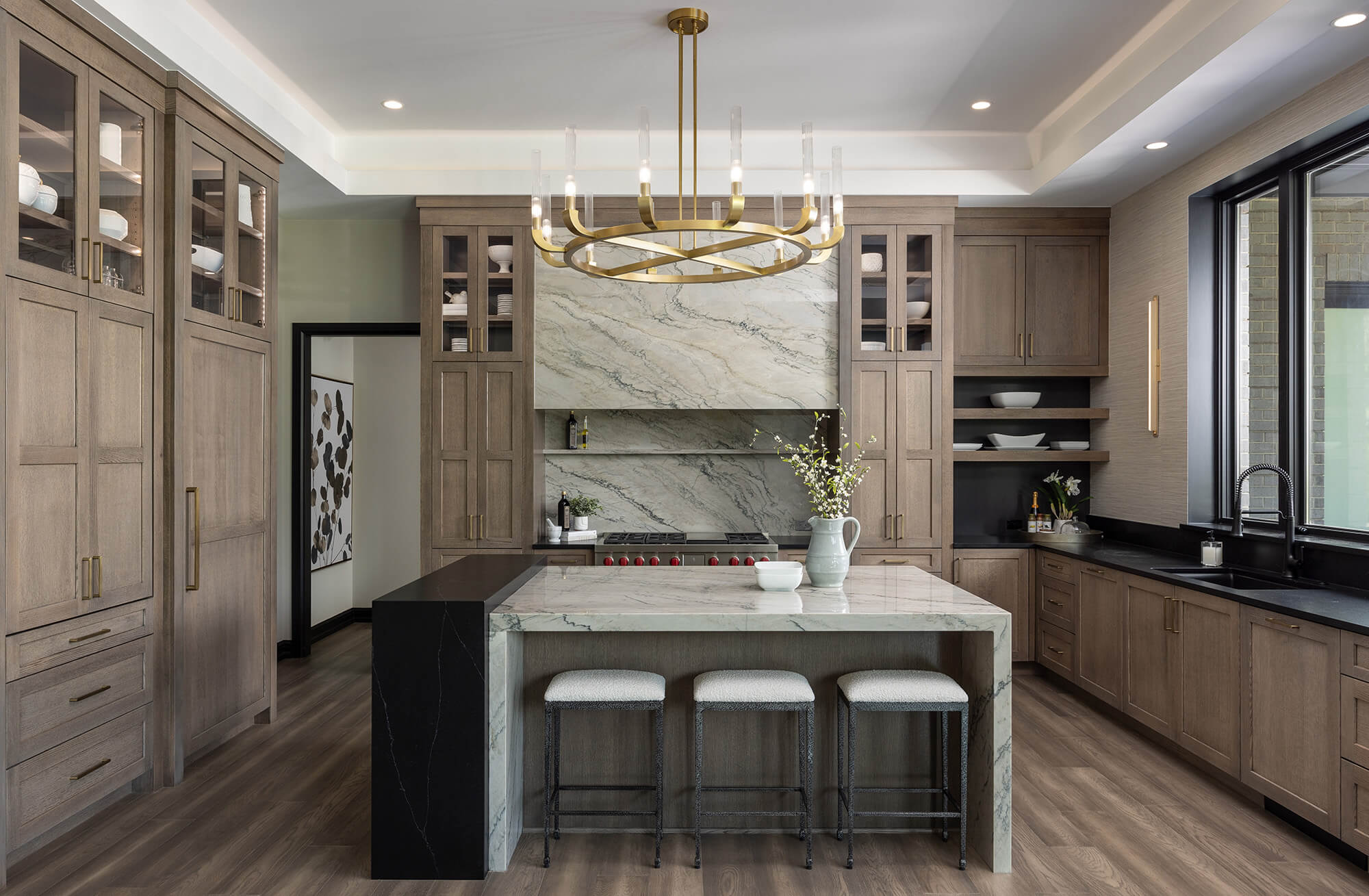 A gray-stained kitchen with a large quartz hood and a kitchen island with multiple waterfall countertops.