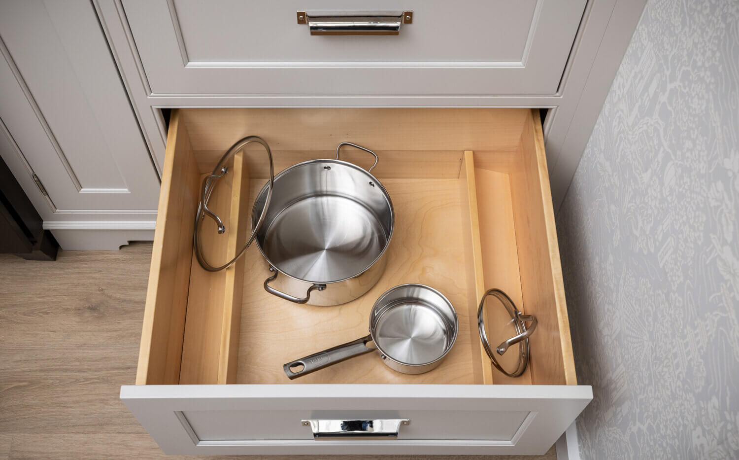 A deep drawer in a kitchen with dividers for lid storage for organizing pots & pans.