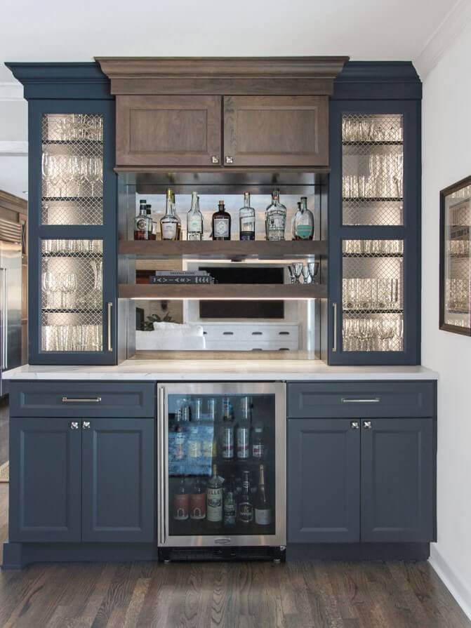 A beverage center area in a kitchen that uses wired mesh inserts and internal cabinet lighting to display what is stored in the cabinets.