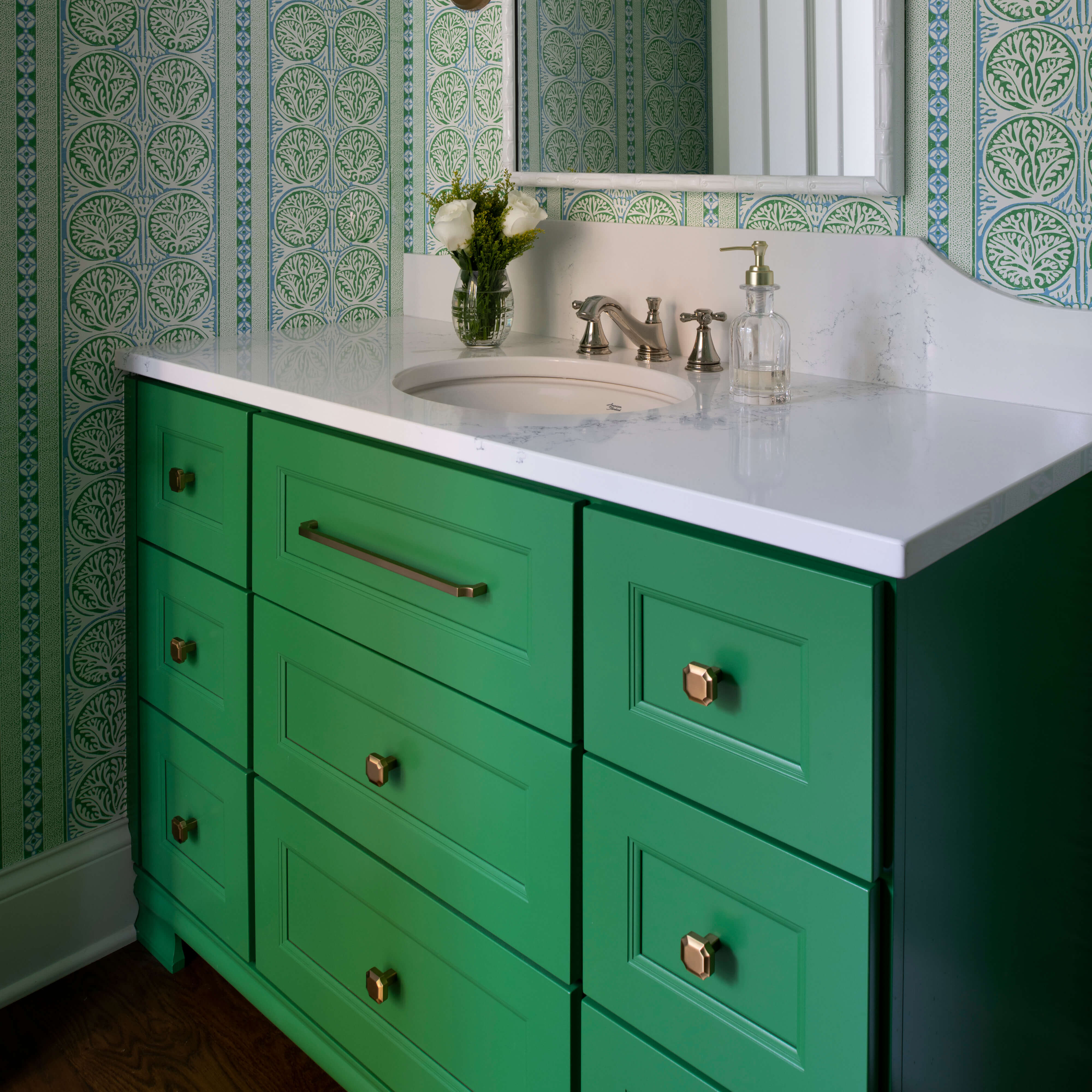 A vibrant, watermelon green bathroom vanity from Dura Supreme Cabinetry with elegant green wallpaper and brushed brass accents.