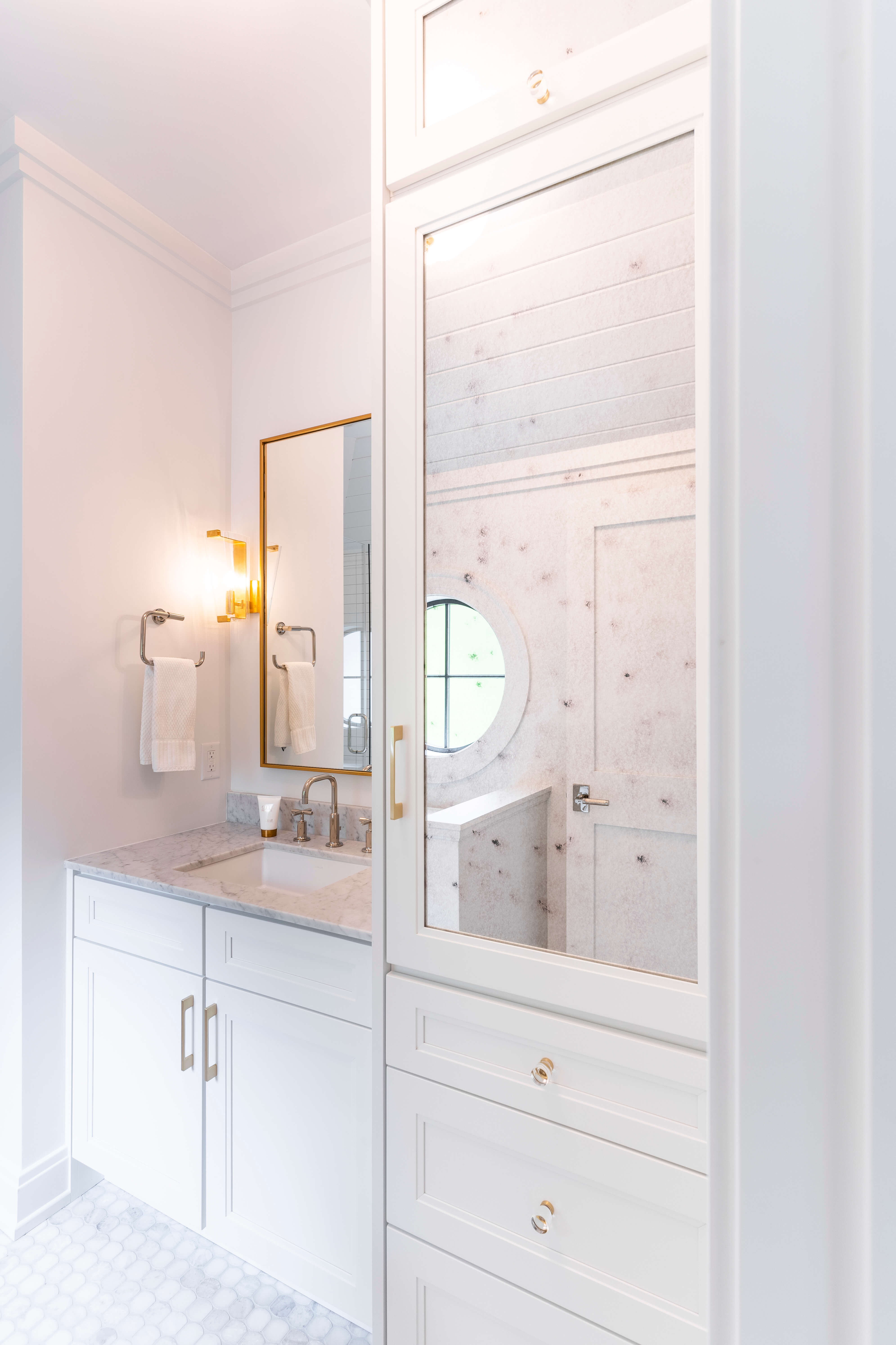 A bright all white bathroom design with a mirror insert in a tall linen cabinet to help the small room feel more spacious.