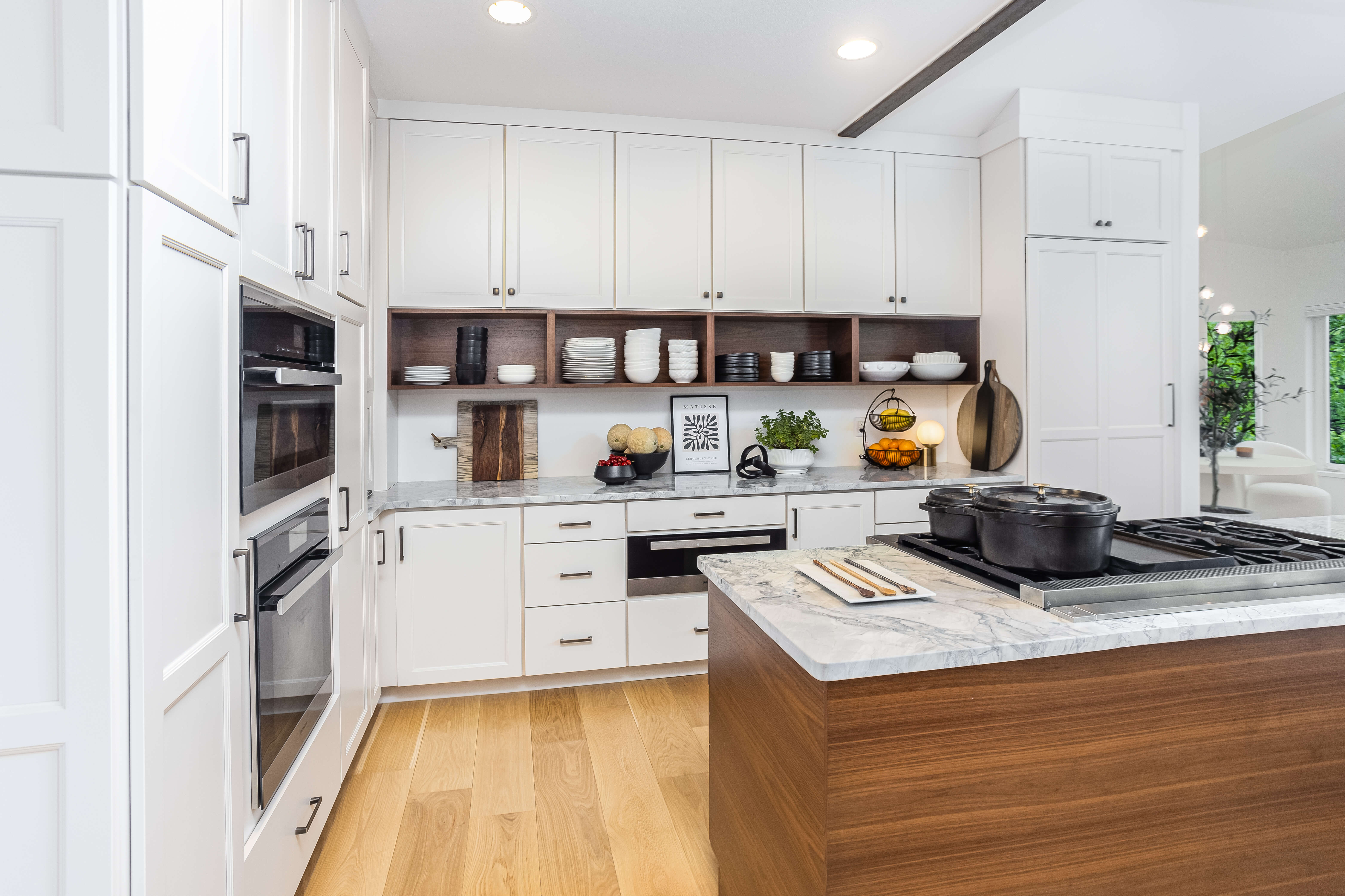 A stunning bright white kitchen with a contrasting medium stained wood for the open cabinets that match the kitchen island.