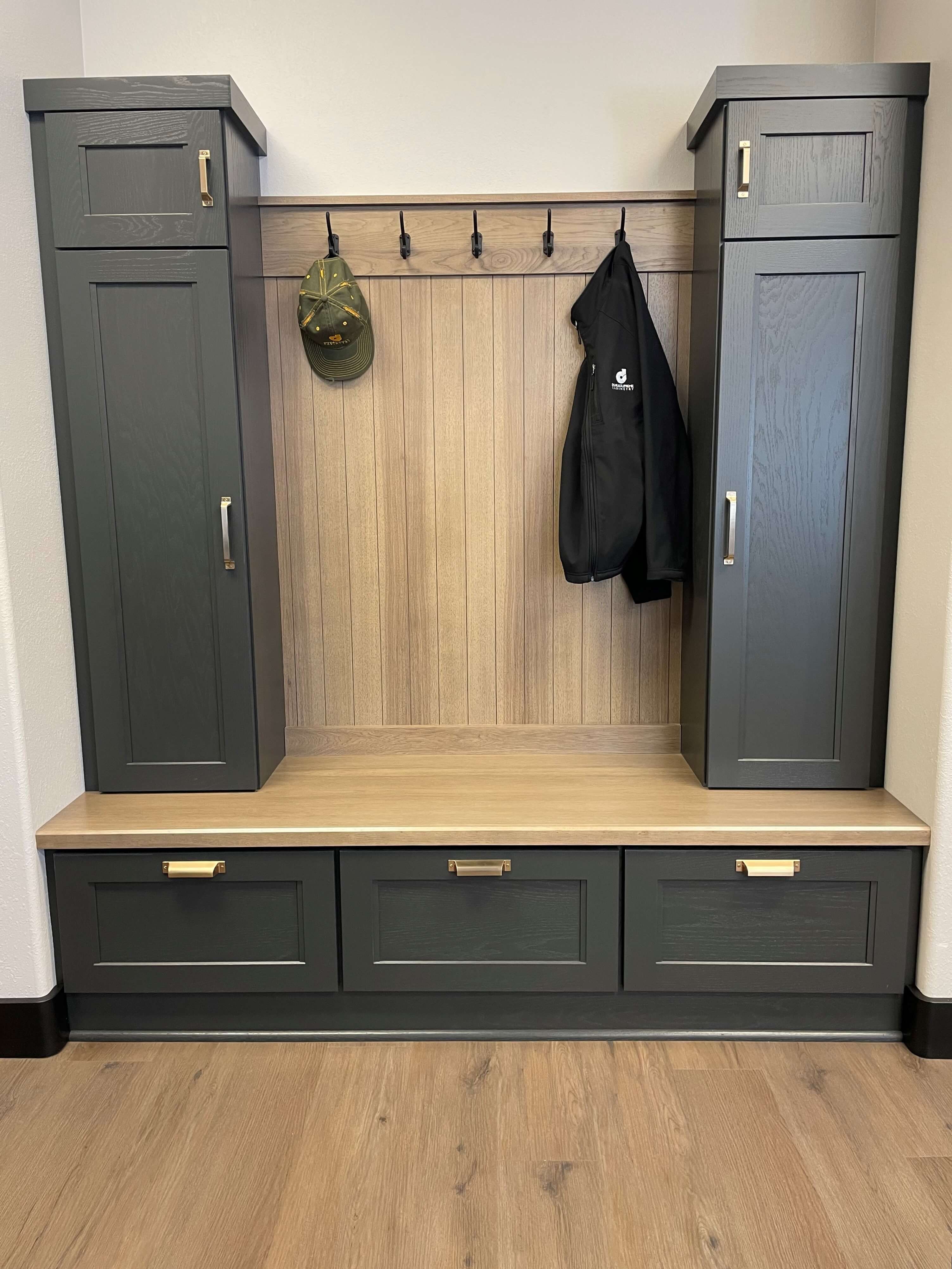 An entry way nook with two tower mudroom lockers and a boot bench framing the coat hook space with a beadboard panel shown with a painted oak finish.