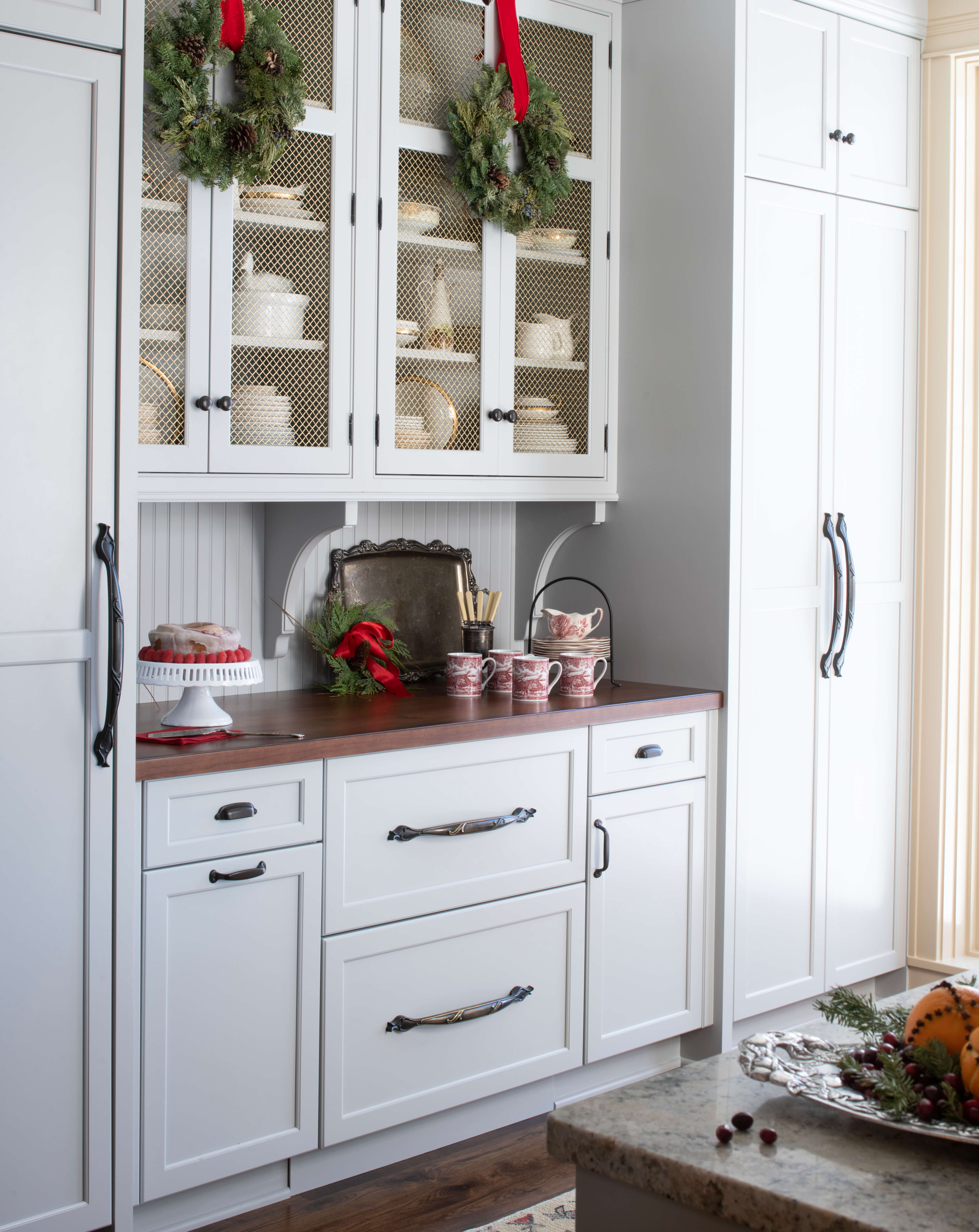 A stunning old English style kitchen with light gray painted cabinets and wire mesh inserts for the accent doors displaying the dishware collection.