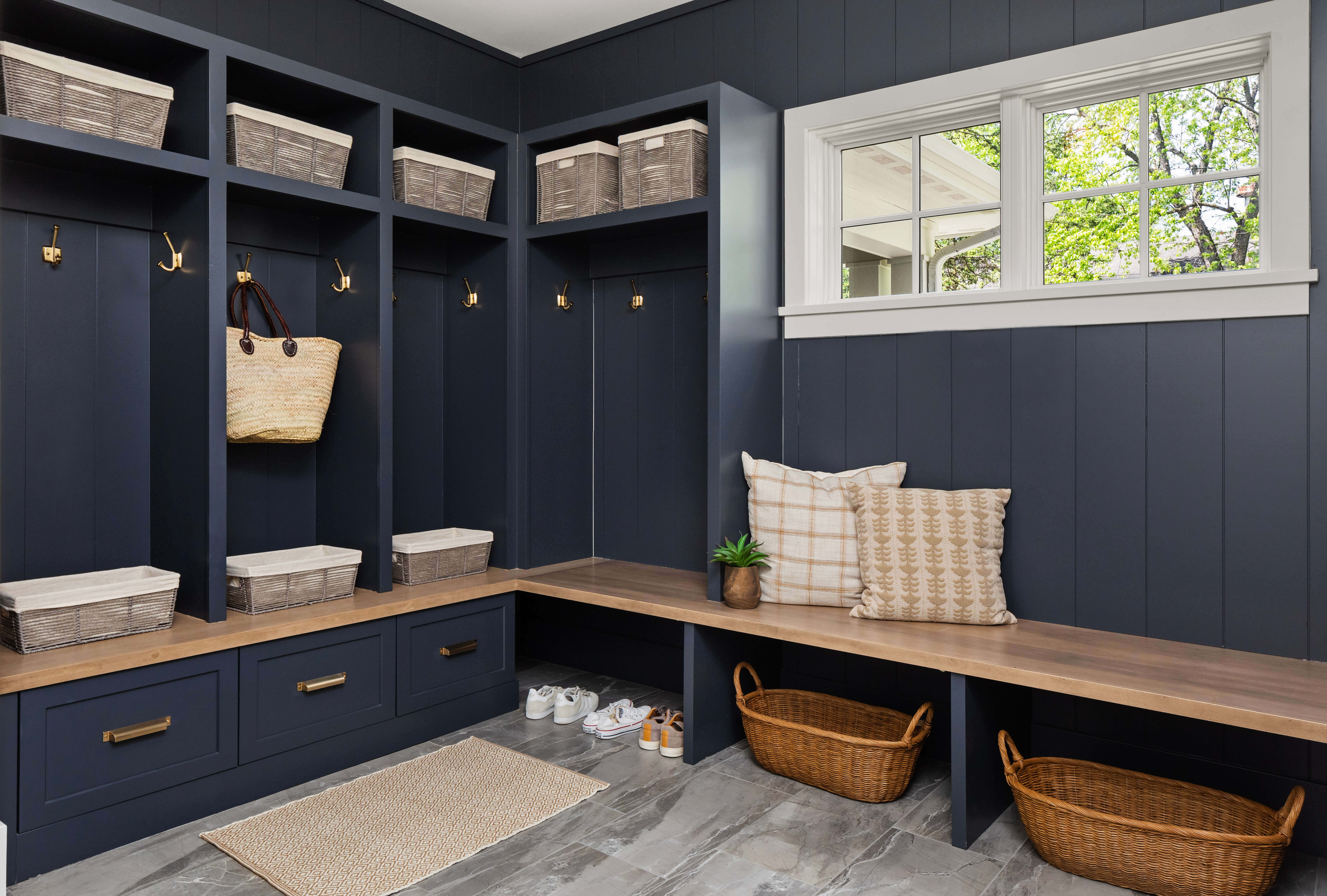 A nautical styled mudroom entryway with dark navy blue painted locker cabinets and shiplap wall with a light wood stain for the boot bench.