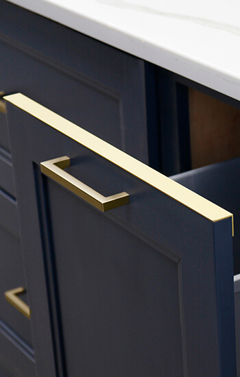 A pull-out trash can cabinet with a protective metal drip edge on the top of the cabinet door.