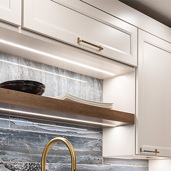 A close up of integrated lighting under a floating shelf and under wall cabinets.