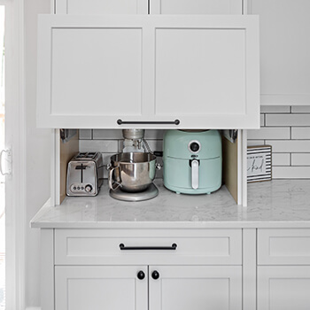 A lift-up cabinet door showing the inside to a frameless, full-access cabinet with hidden appliance storage at counter level.