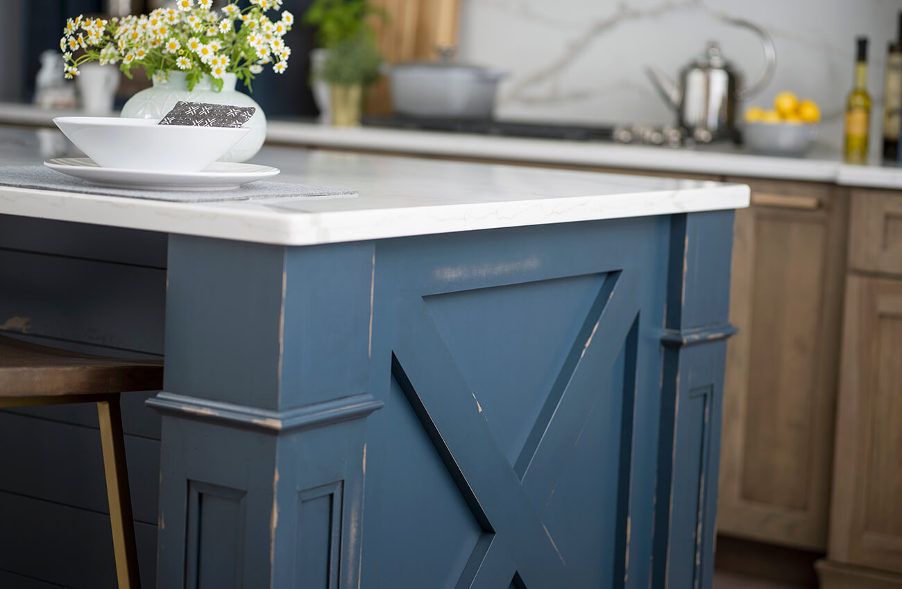 A custom distressed kitchen island with a modern farmhouse style featuring column posts and an X end cap.