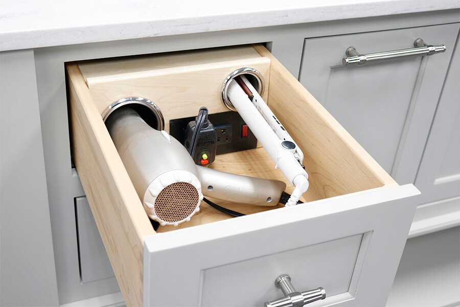 A bathroom vanity drawer with a power station and storage cups for powering and storing hair dryers, flatteners, and curling irons.