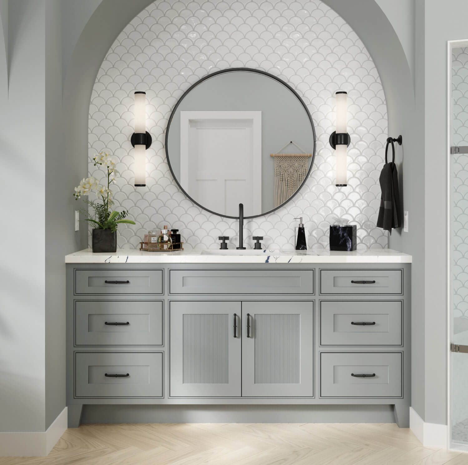 A gray painted bath vanity with reeded cabinet doors and a shallow shaker style tucked into an Arched wall with black faucet and hardware accents.